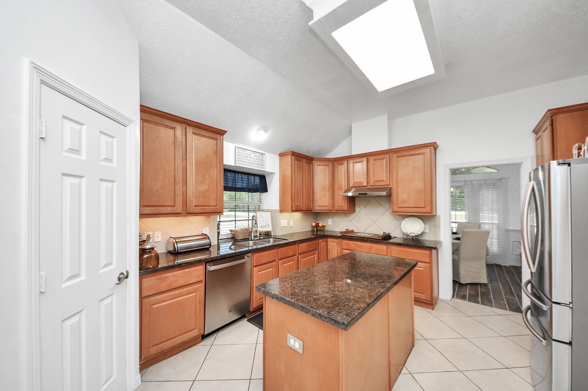 Kitchen with warm wood cabinets, granite counters, a central island, and stainless steel appliances.