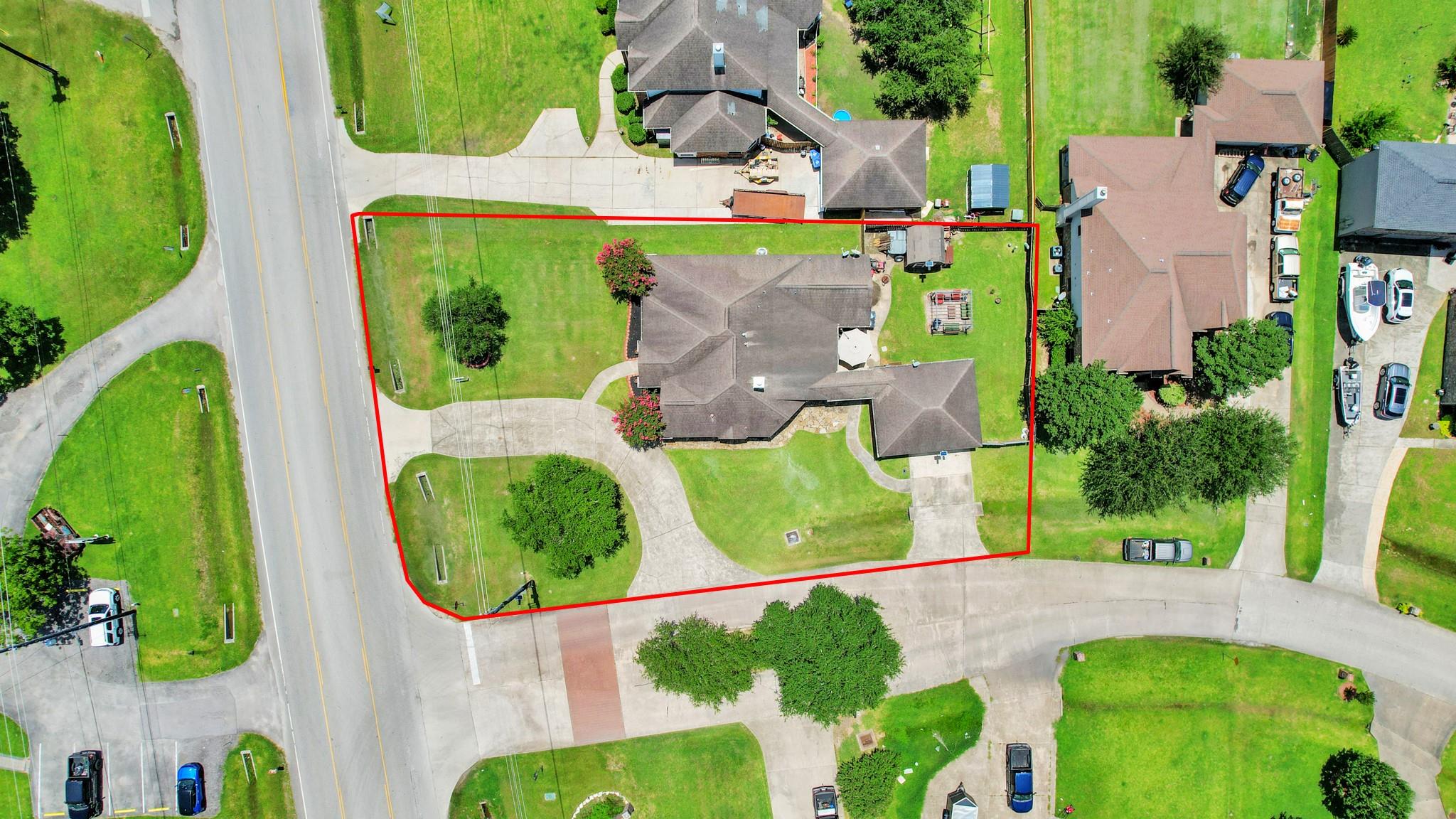 Aerial view of a home and its red-outlined lot, with curved driveways beside the road.