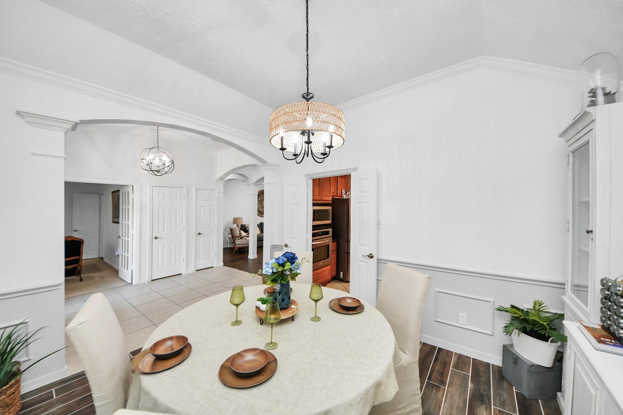 Dining room with a round set table, woven chandelier, and arched openings to adjoining rooms.