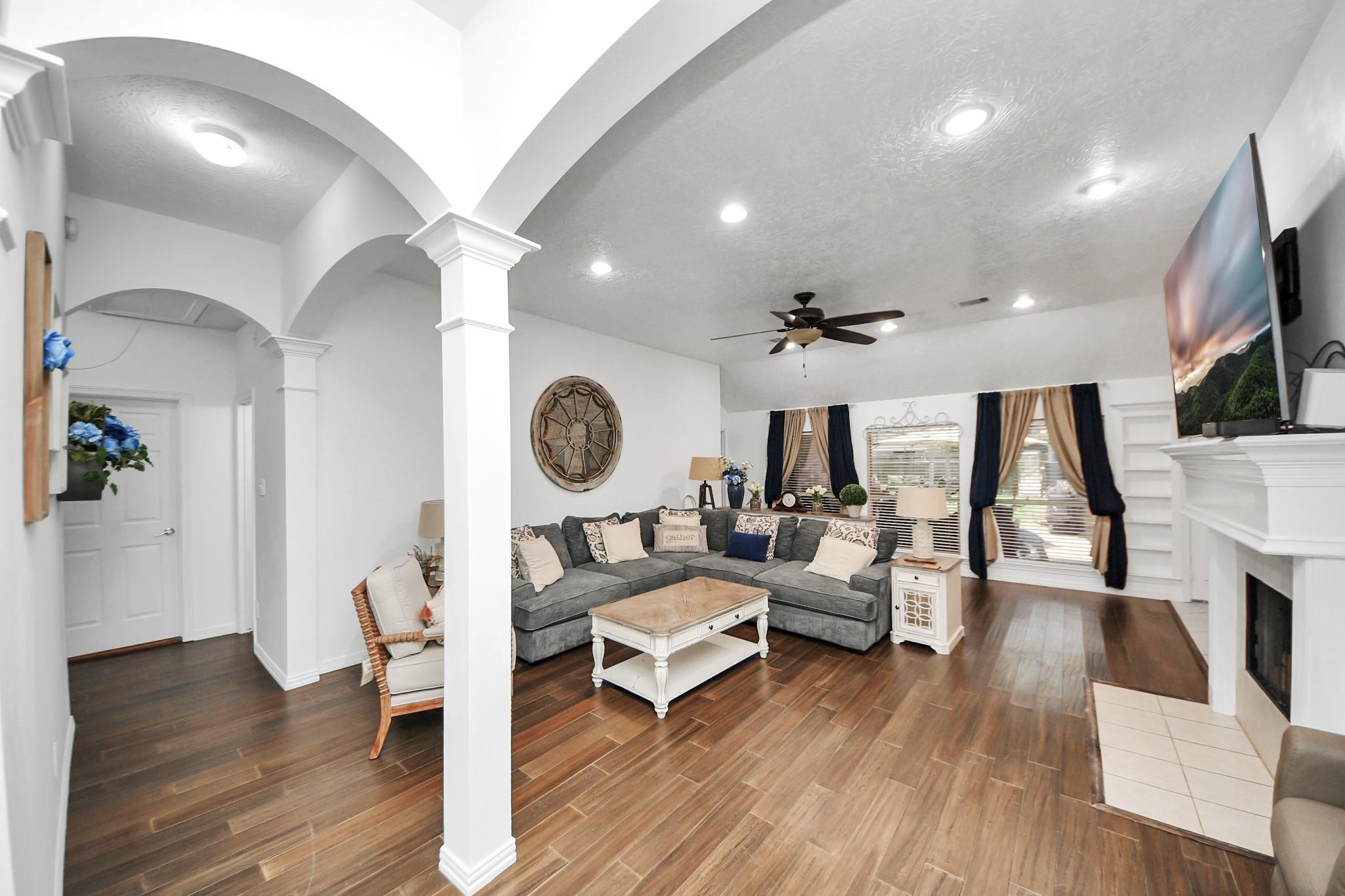 Living room with a gray sectional, arched openings, wood-look tile floors, and a white fireplace.