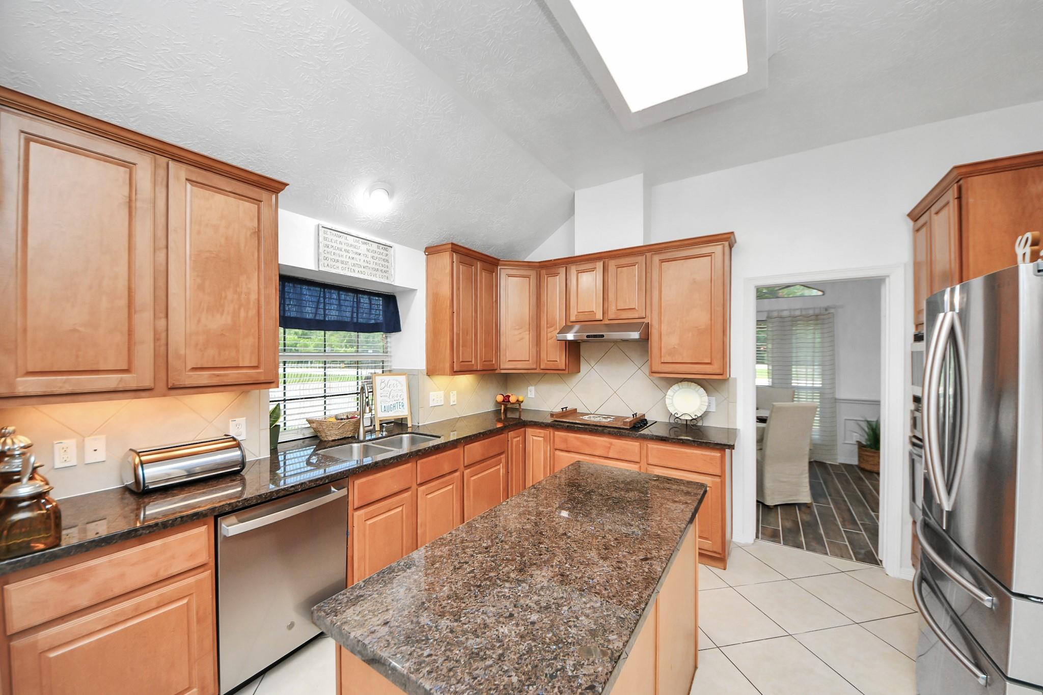 Kitchen with warm wood cabinets, granite island, stainless steel appliances, and a skylight.