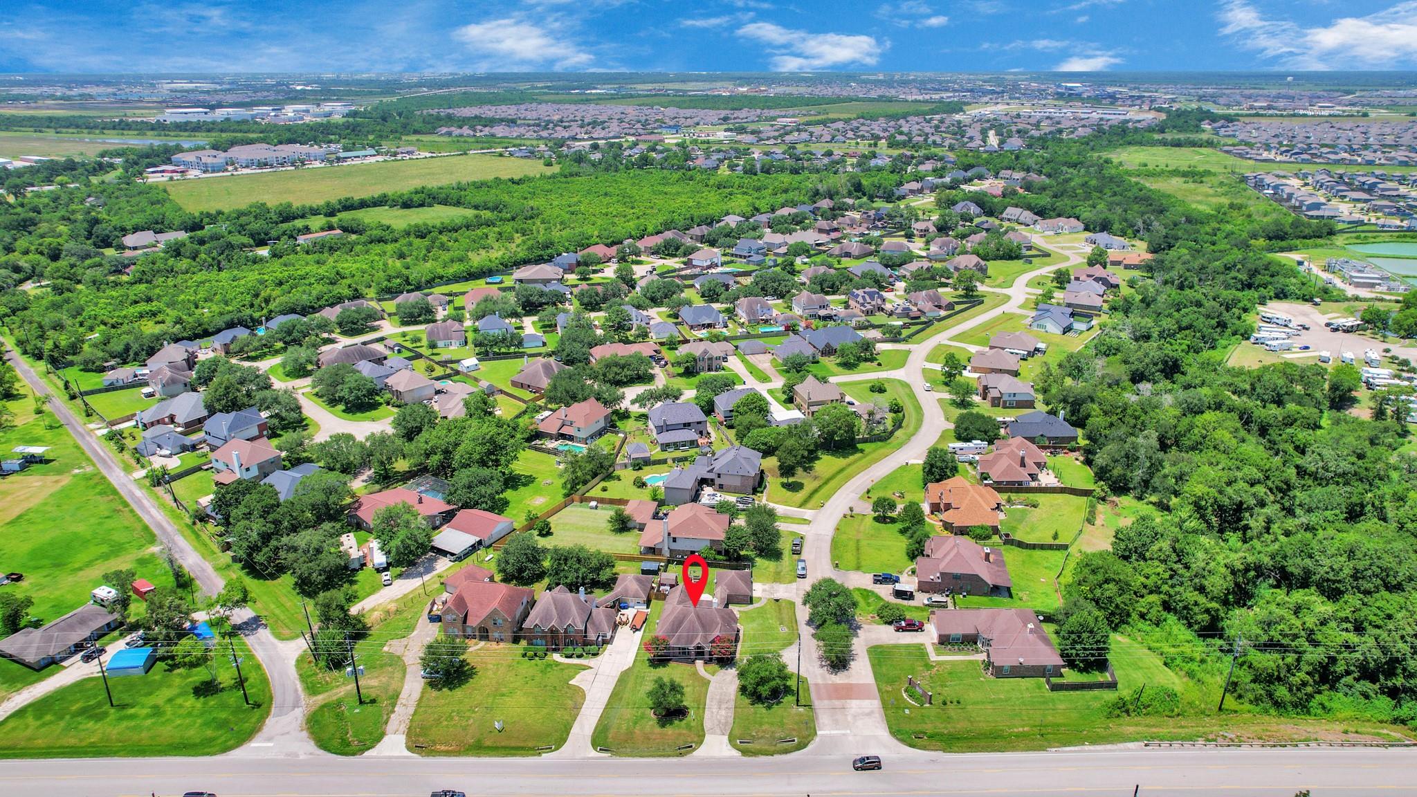 Aerial view of a leafy neighborhood with a red map pin marking a house near the foreground.