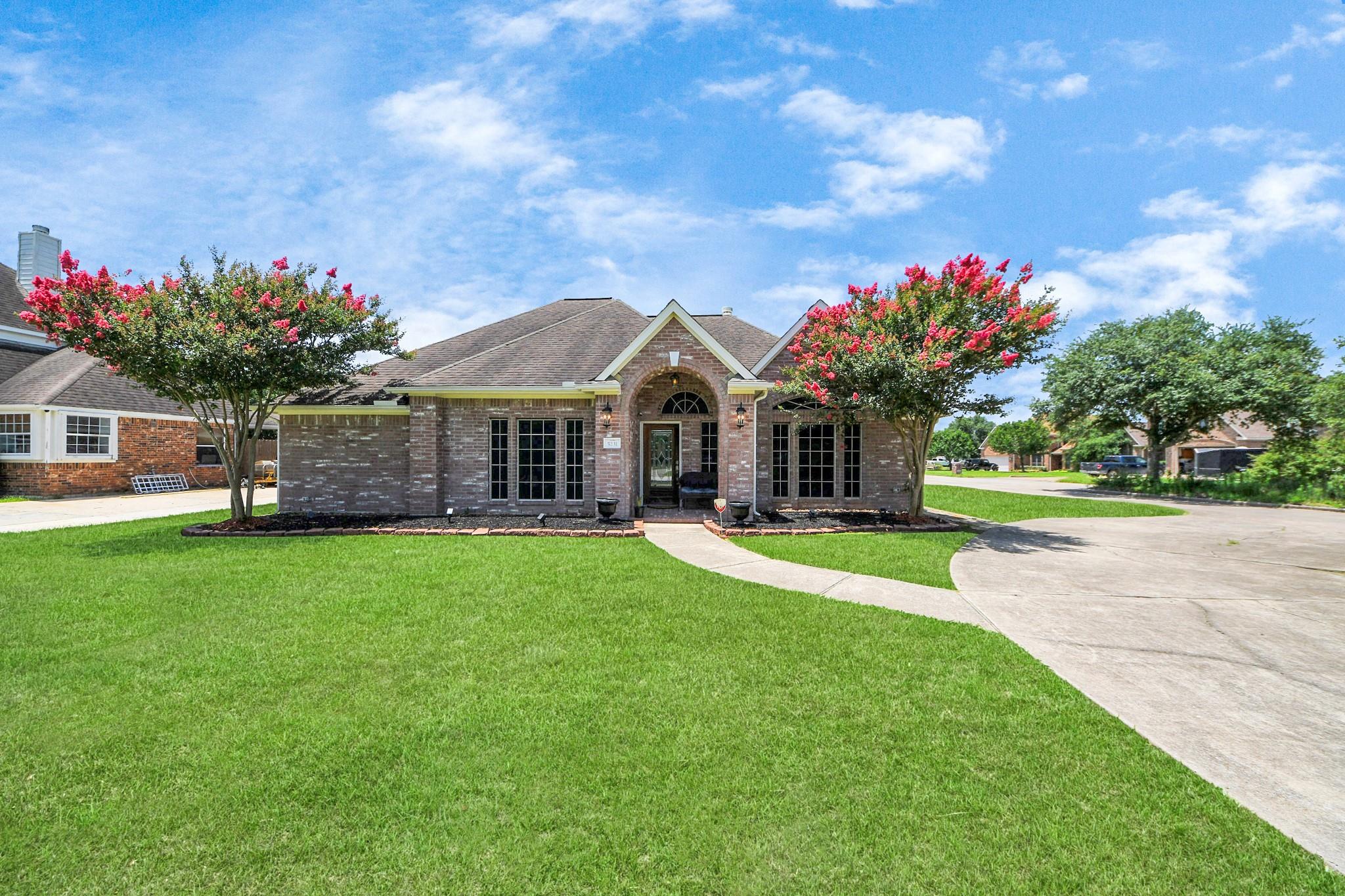 Brick home with an arched front entry, flowering trees, broad lawn, and curved driveway.