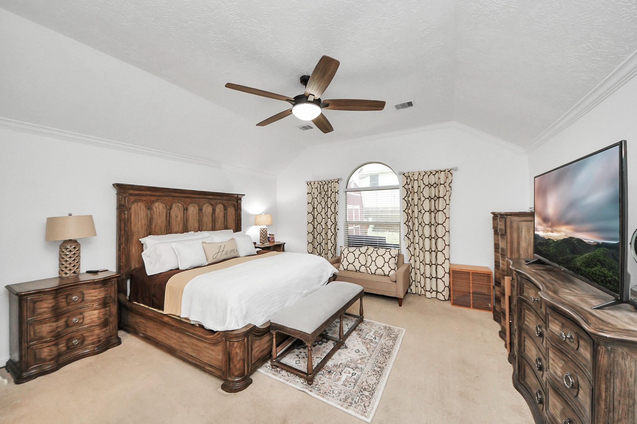 Bedroom with a carved wood bed, matching furniture, patterned rug, and arched window.