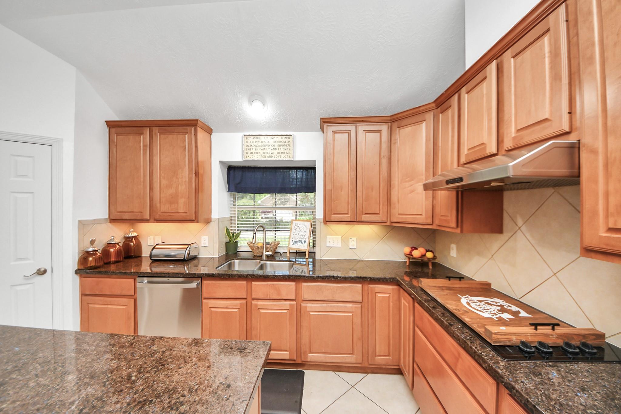 Kitchen with warm wood cabinets, dark granite counters, and a gas cooktop beneath a stainless hood.
