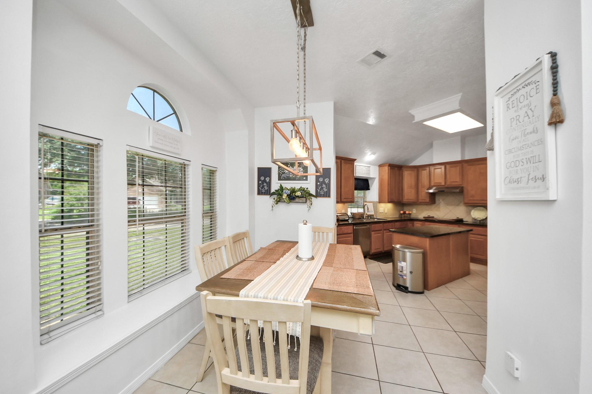 Dining area with a long wood table beside the kitchen, which has warm wood cabinets and a central island.