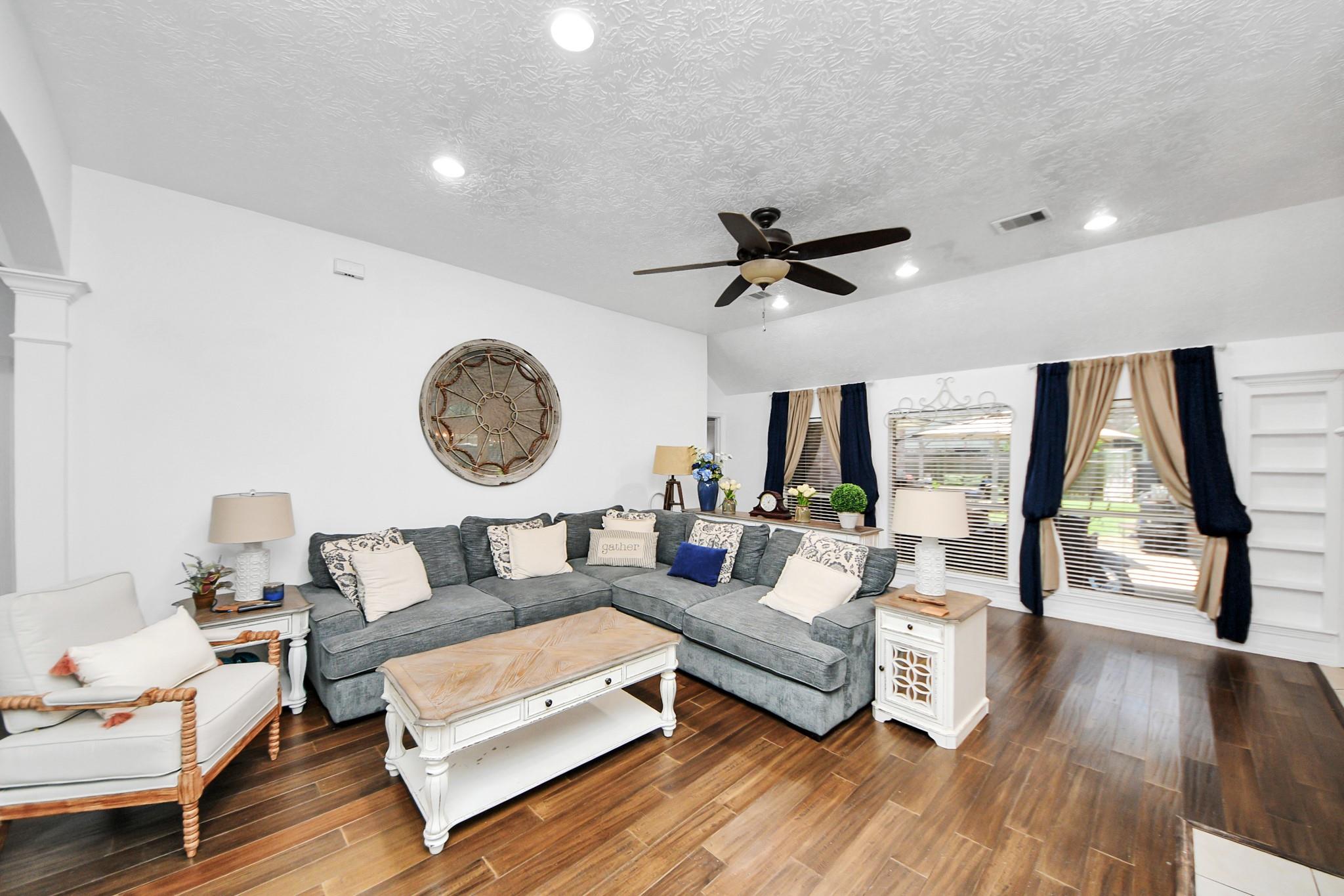 Living room with a gray sectional, white furniture, dark wood floors, and large curtained windows.