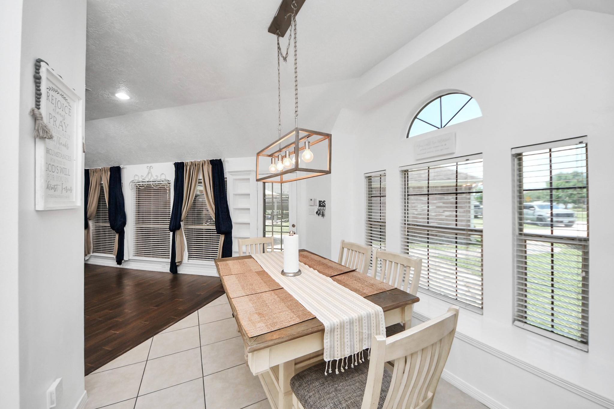 Dining room with a wood table, white chairs, geometric pendant light, and tall windows with blinds.