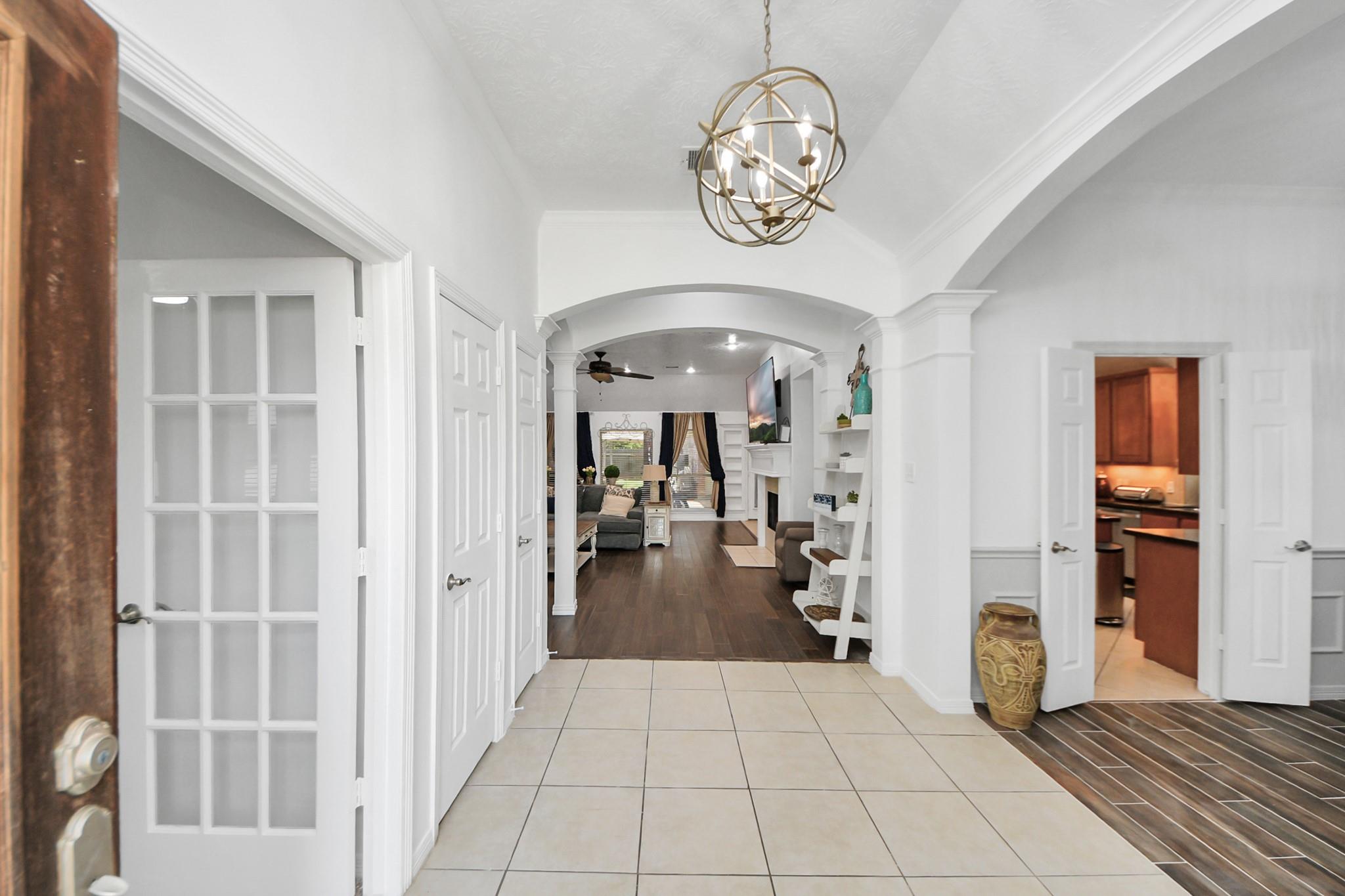 Entry hall with a globe chandelier opening into an arched, furnished living room.