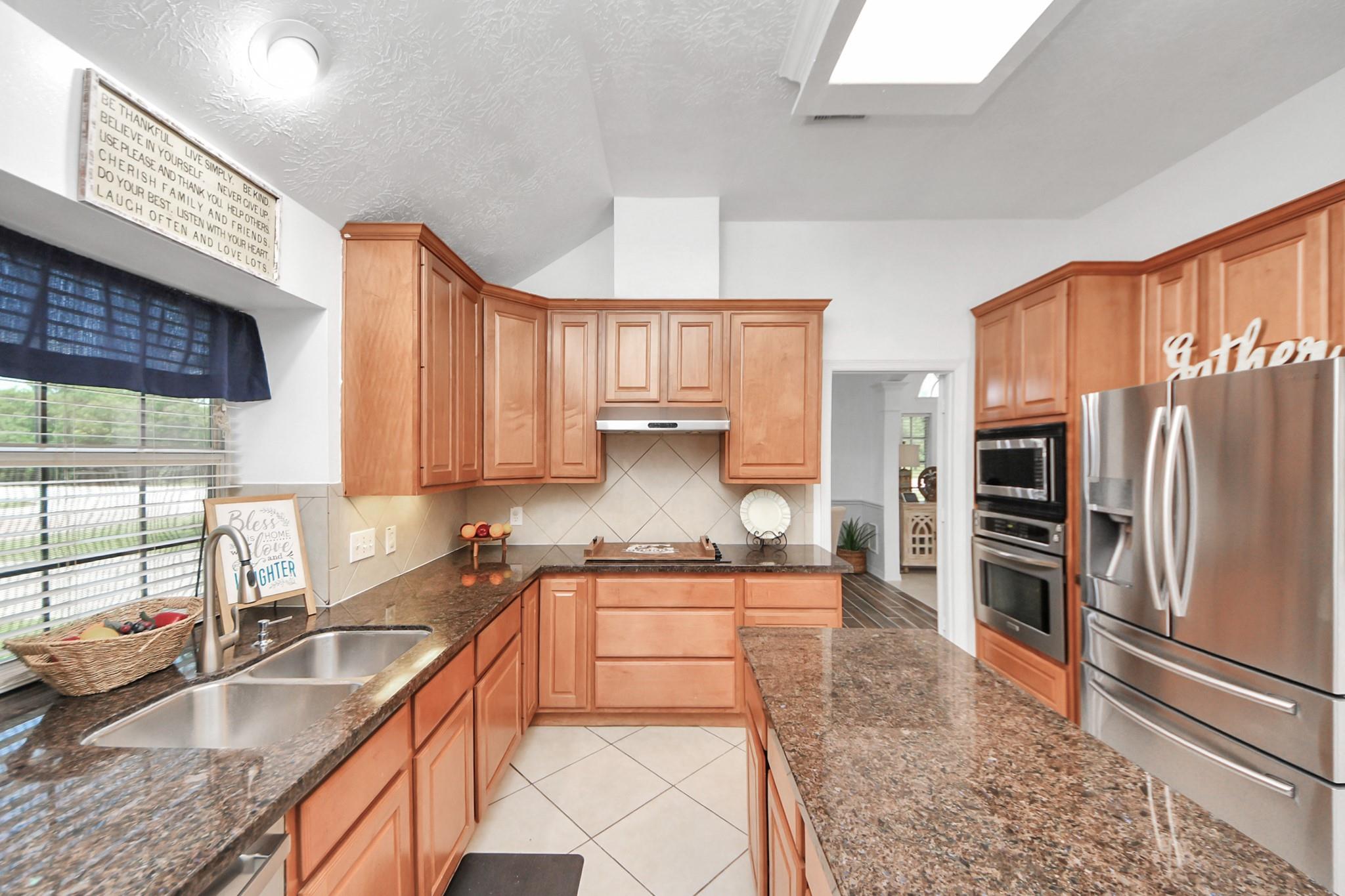 Kitchen with warm wood cabinets, granite counters, a long island, and stainless steel appliances.