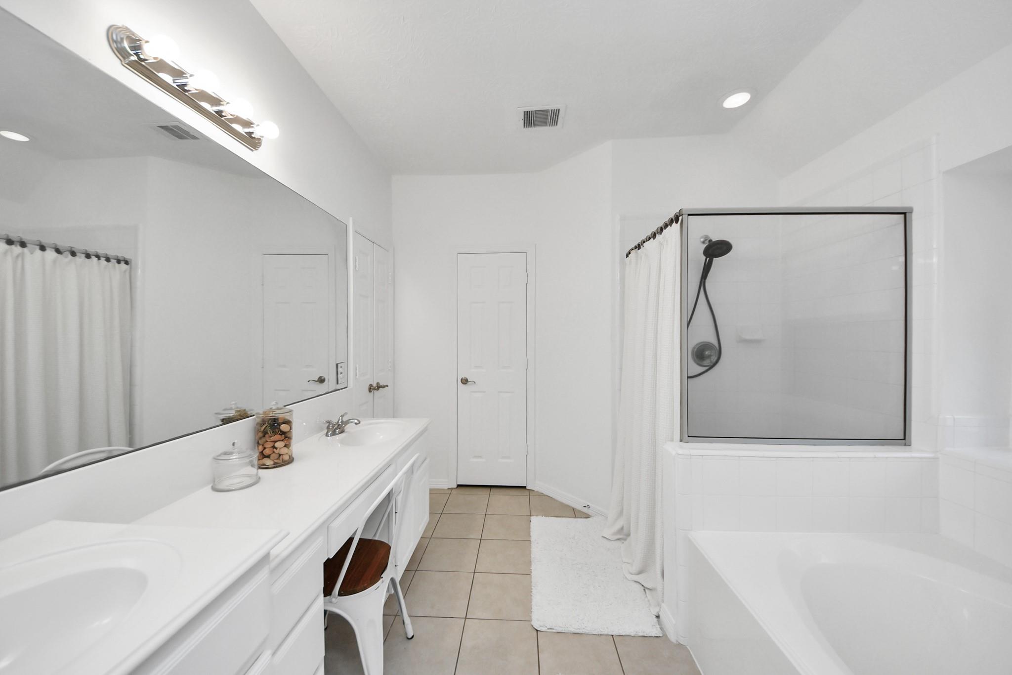 Bright bathroom with a long double-sink vanity and a glass-enclosed tub and shower.