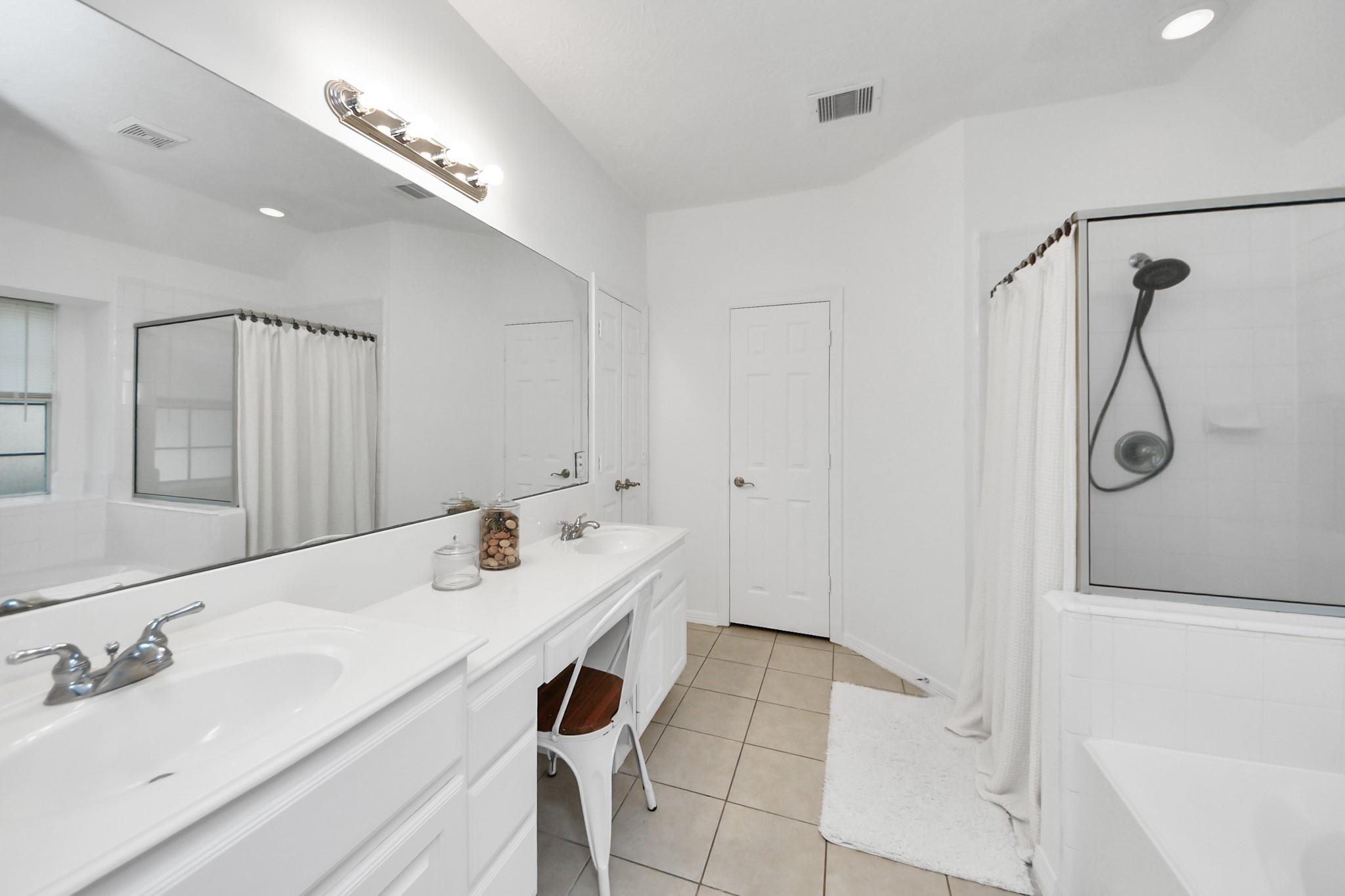 Bright bathroom with a double-sink vanity, large mirror, and curtained shower-tub enclosure.