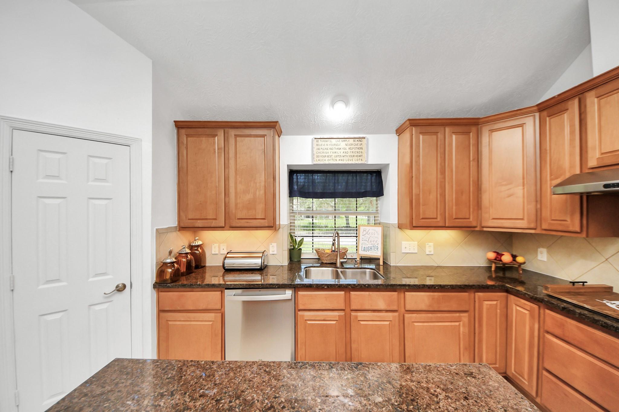 Kitchen with honey-colored cabinets, dark granite counters, and a double-basin sink beneath a window.