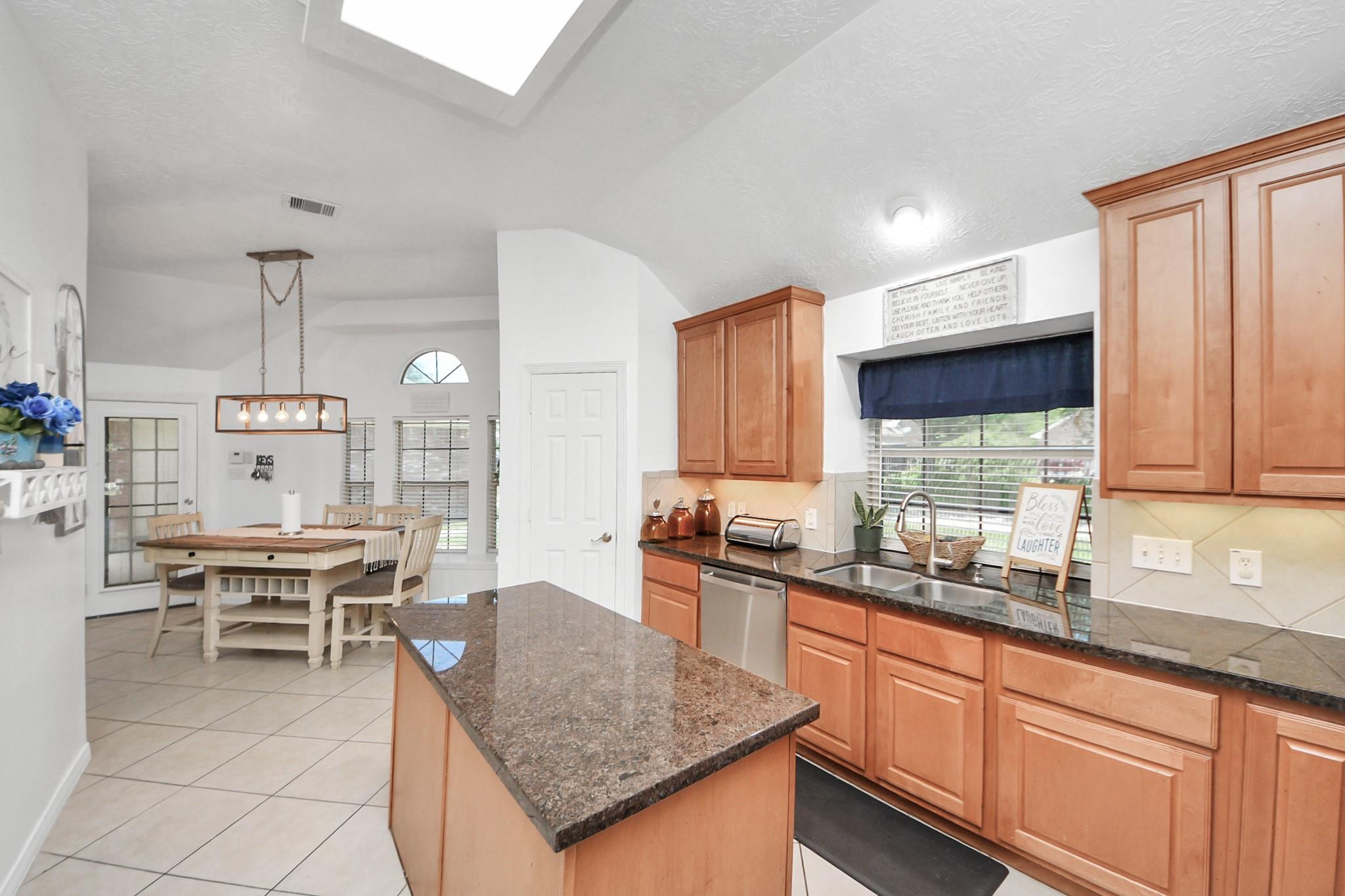 Kitchen with warm wood cabinets, granite island, window-side sink, and adjoining dining area.