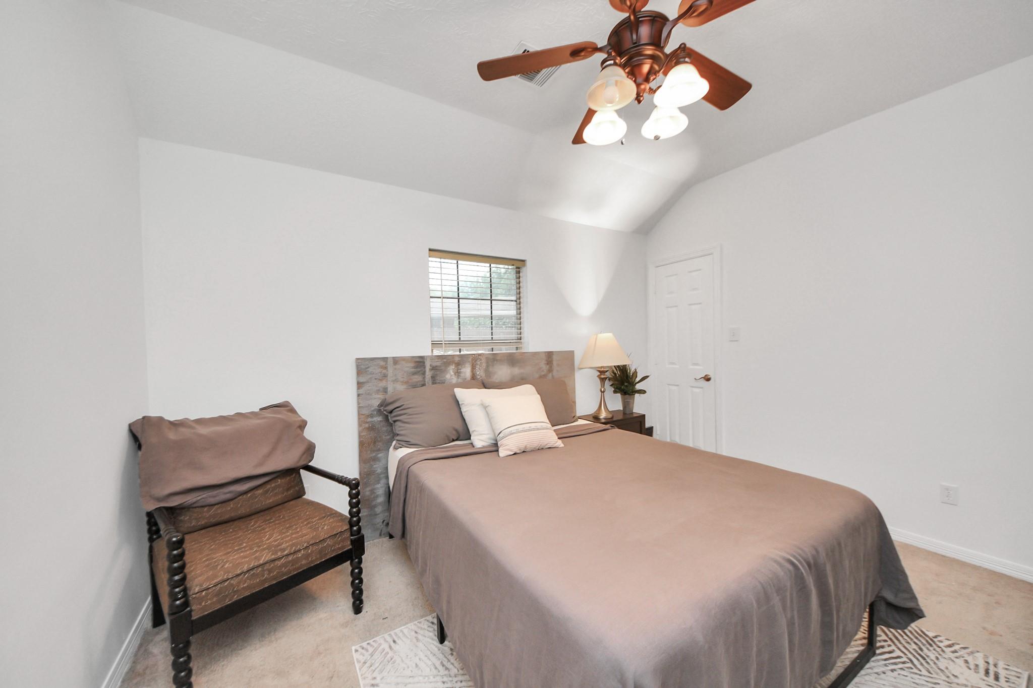 Furnished bedroom with a taupe bed, stone-look headboard, and ceiling fan.