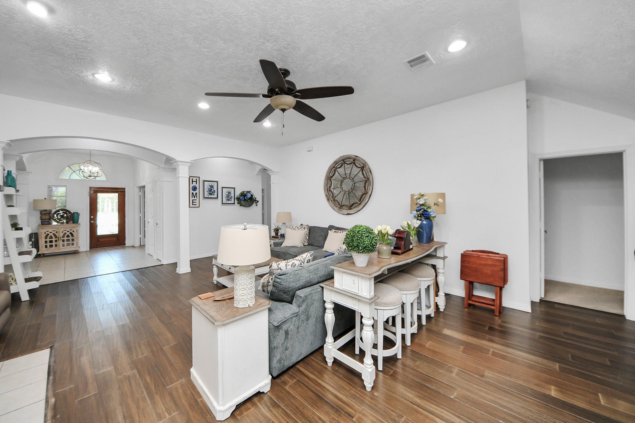 Staged living room with a gray sofa, dark wood-look floors, and an arched opening to the entryway.