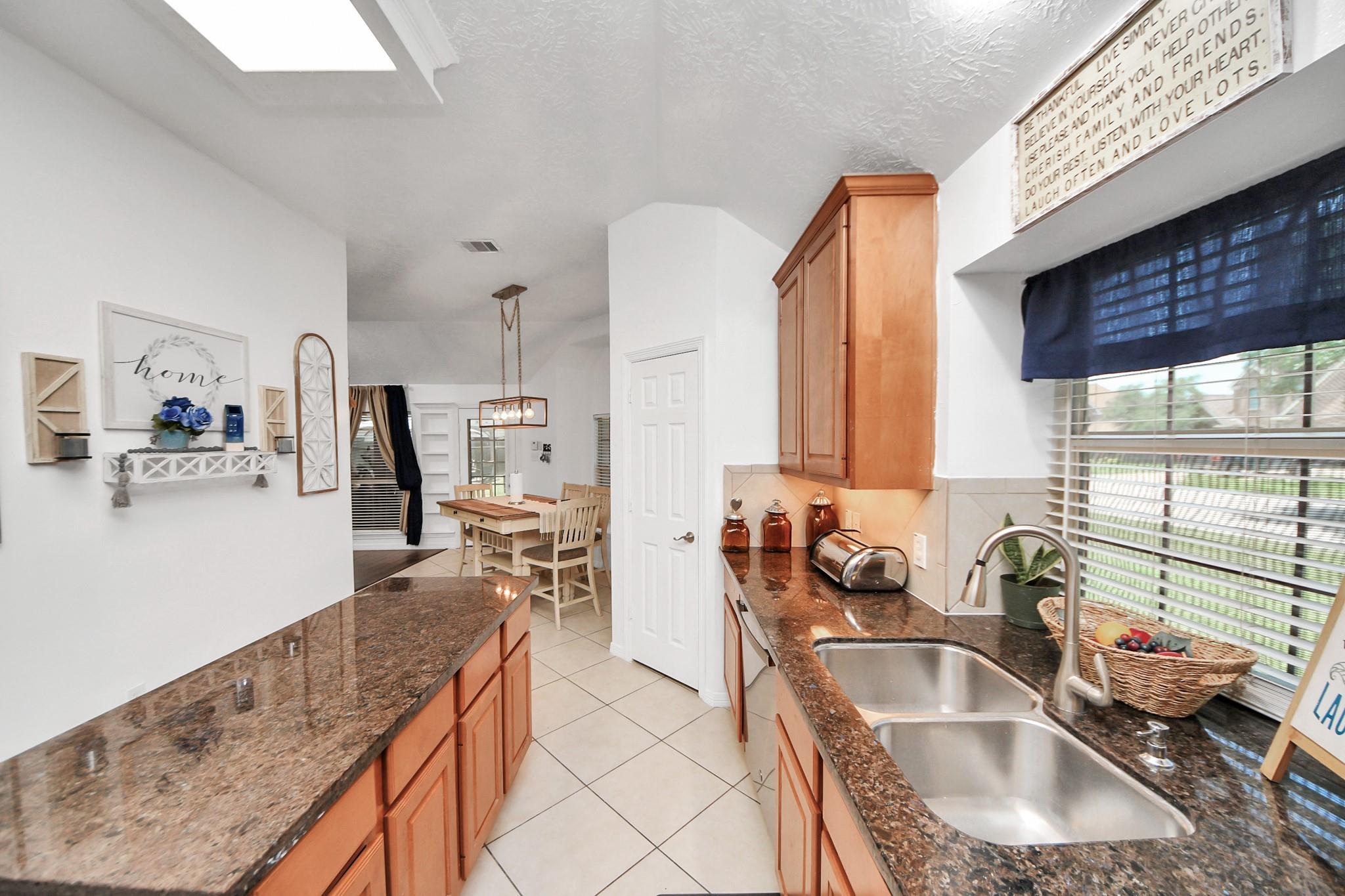 Kitchen with dark granite counters, wood cabinets, a double sink, and dining area beyond.