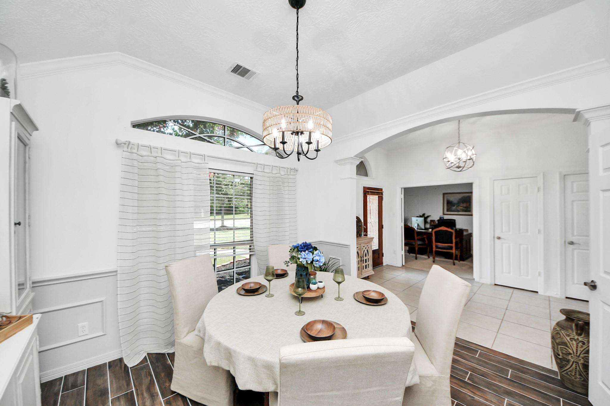 Dining room with a set round table beneath a chandelier and a large curtained window.
