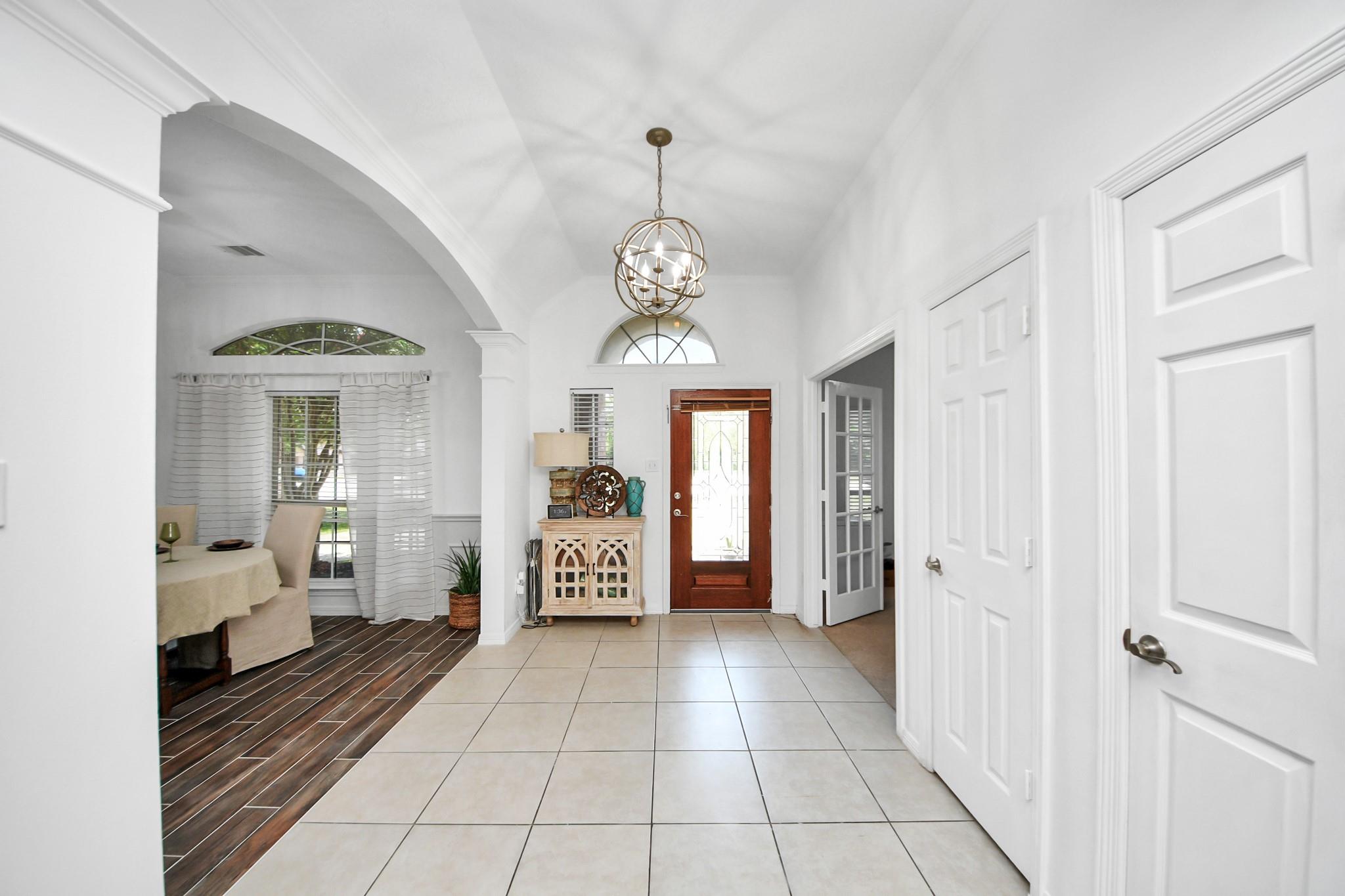 Bright entryway with vaulted ceiling, tiled floor, globe pendant, and wood-and-glass front door.