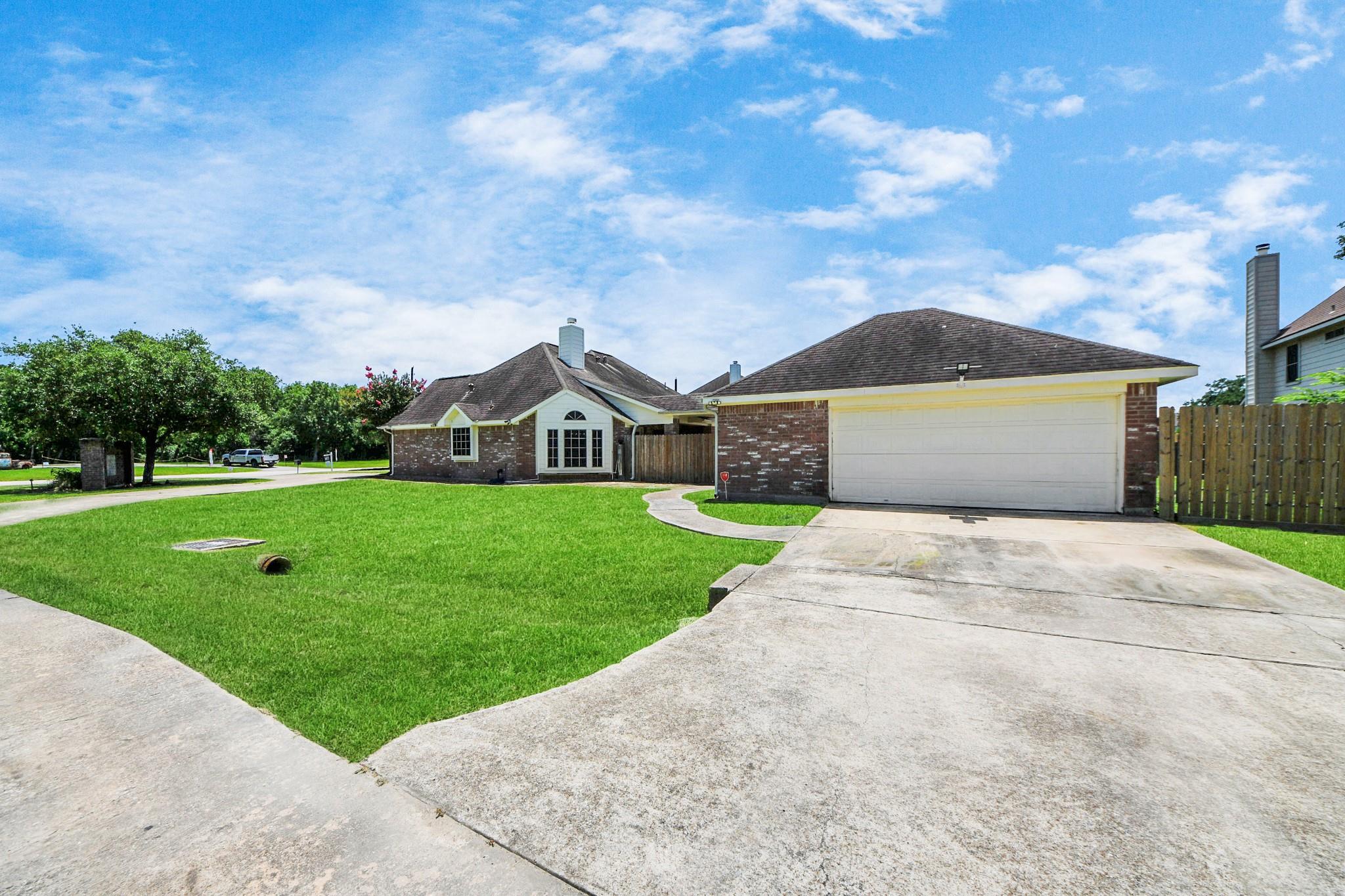 Brick house with a two-car garage, wide concrete driveway, and green front lawn.