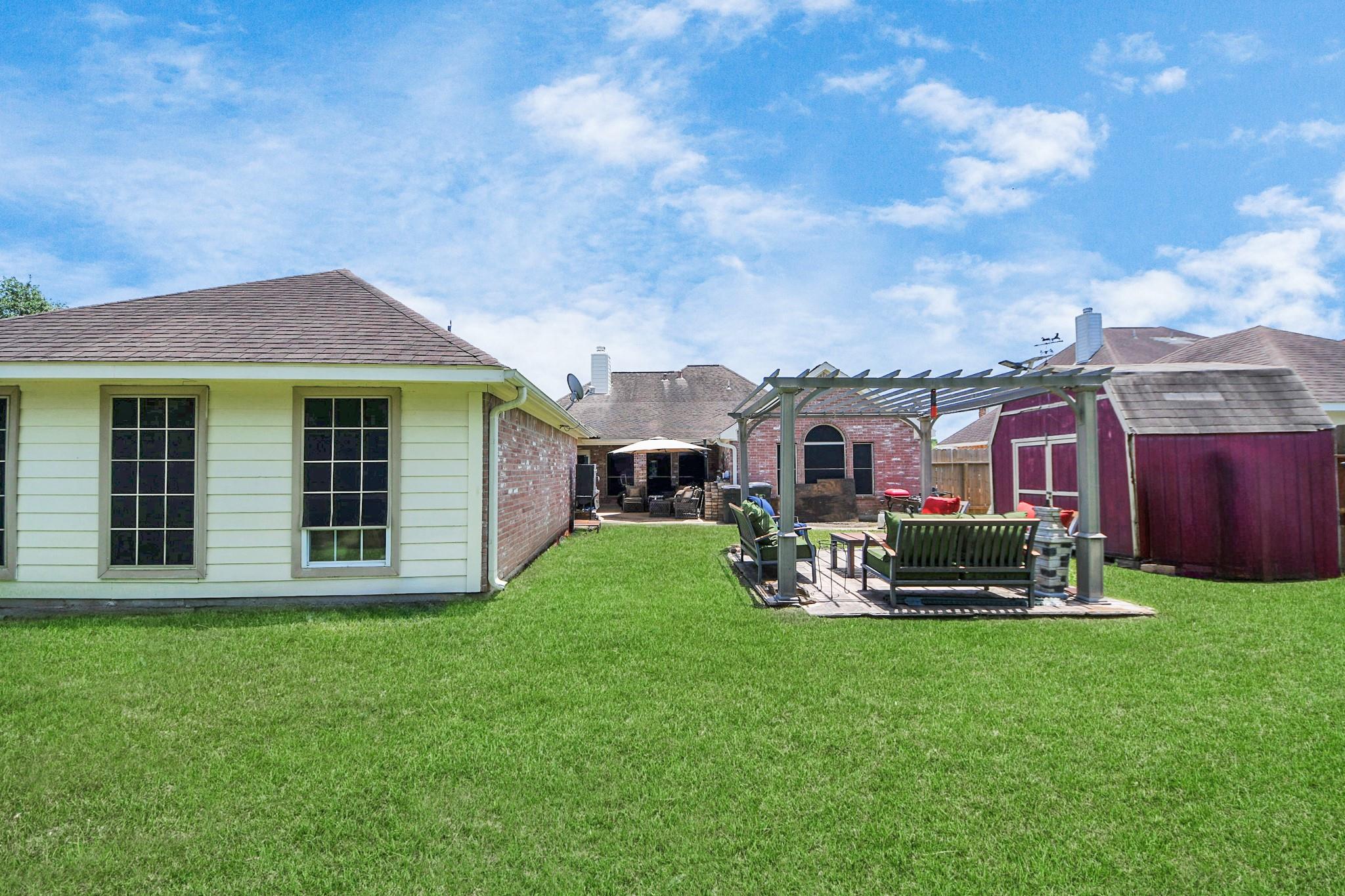 Backyard with a broad lawn, pergola-covered seating patio, and red storage shed.