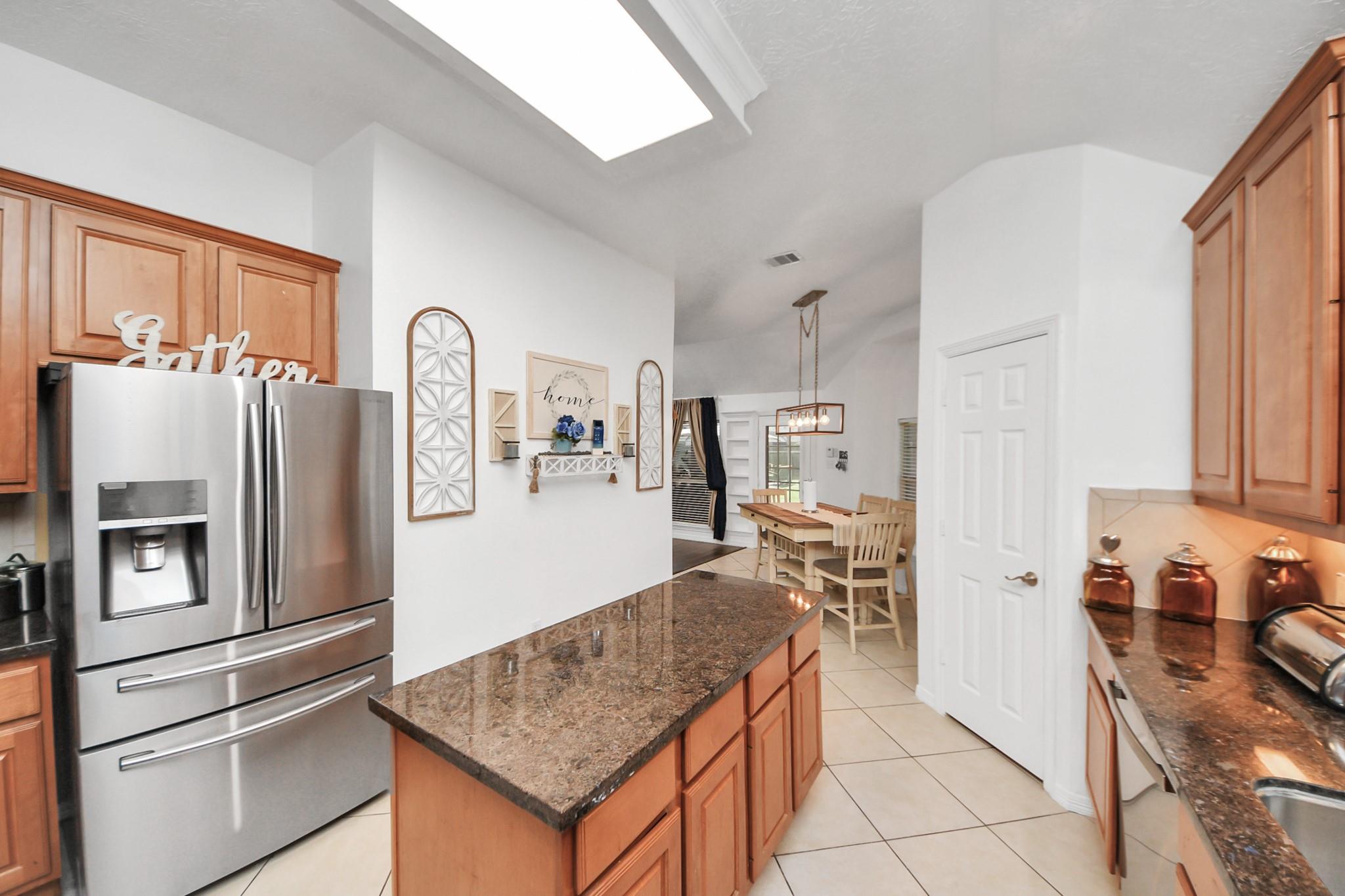 Kitchen with warm wood cabinetry, granite island, stainless-steel refrigerator, and an adjoining dining area.