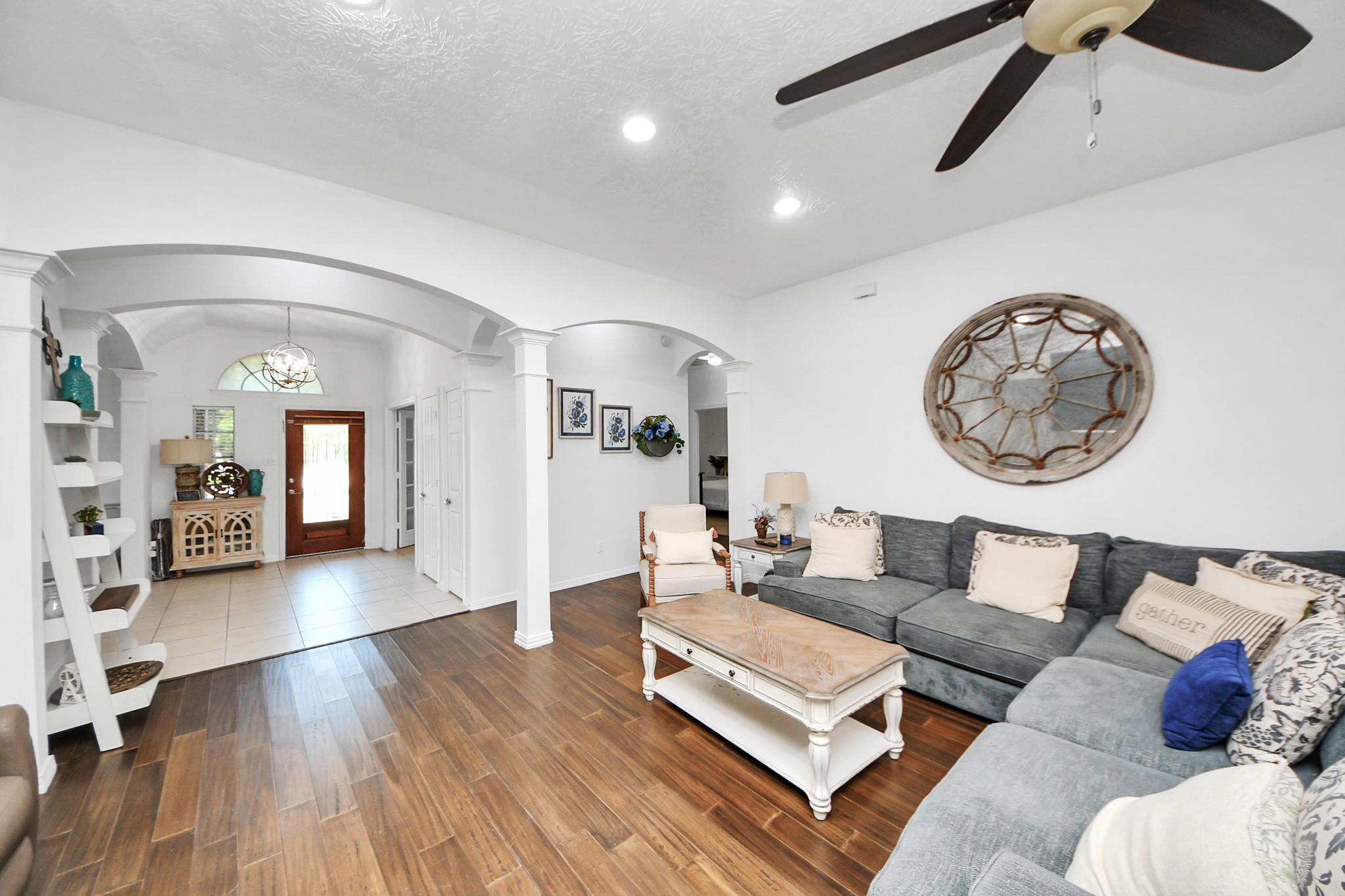 Living room with a gray sectional, wood-look floors, and arched openings to a tiled entryway.