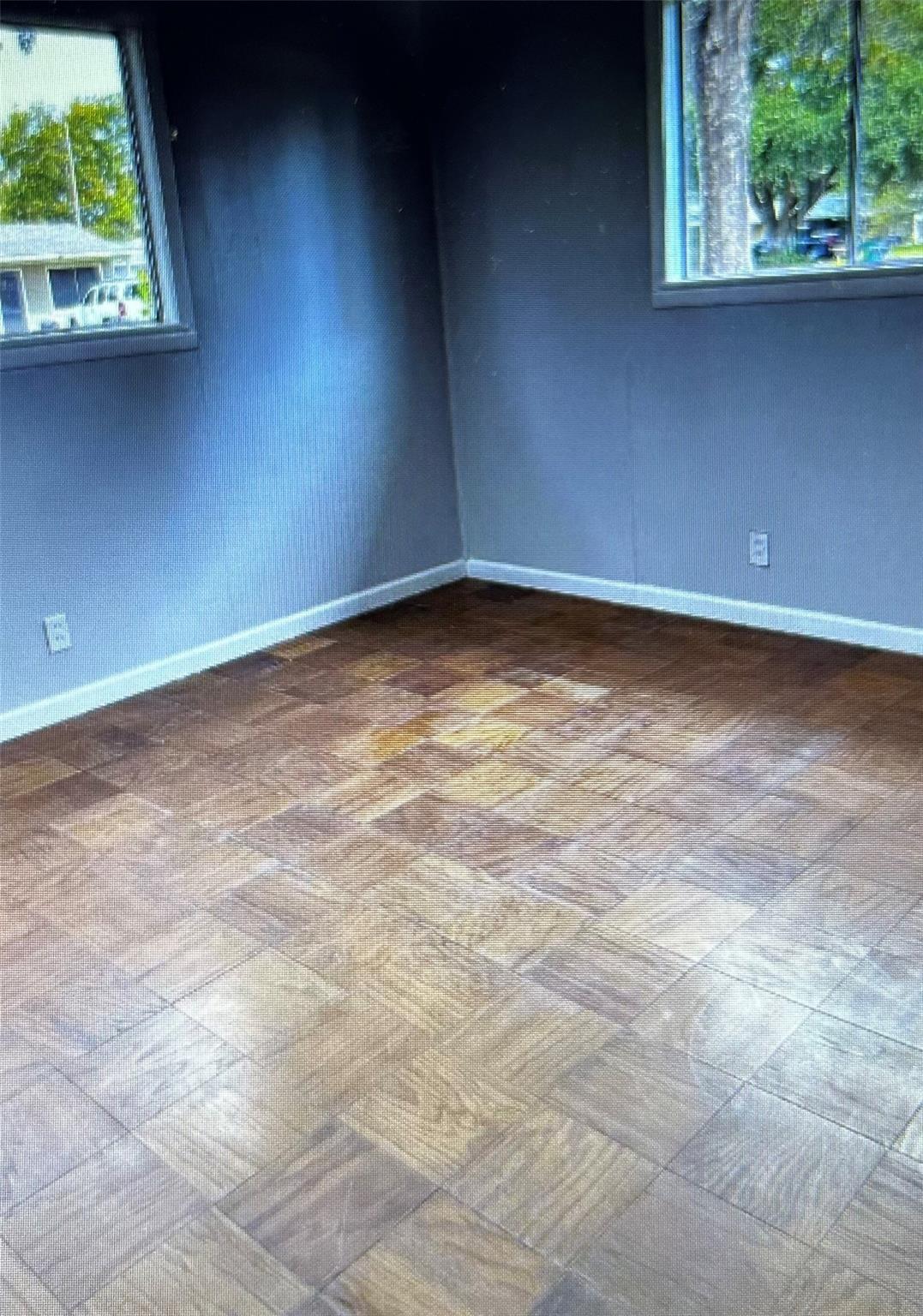 Empty room with gray walls, two windows, and patterned wood parquet flooring.