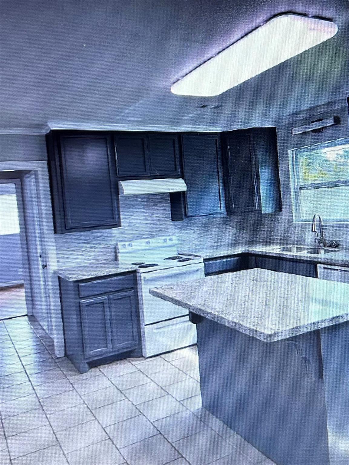 Kitchen with dark cabinets, white electric range, tiled floor, and a large countertop peninsula.