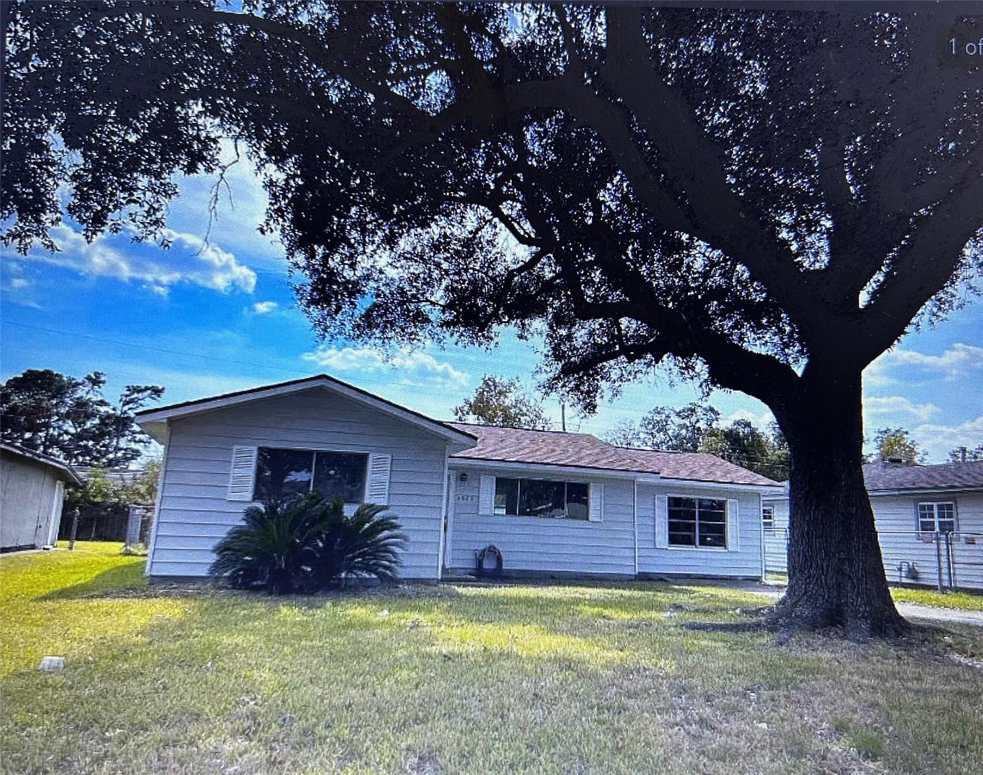 Single-story light-sided house with a large oak tree shading the front lawn.
