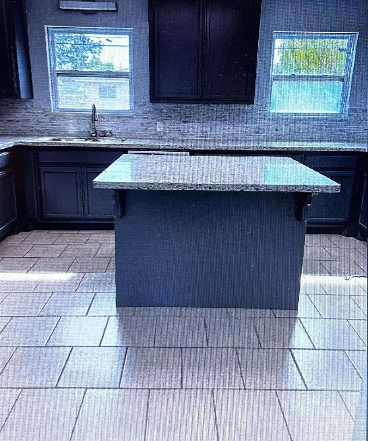 Kitchen with a large stone-topped island, dark blue cabinets, and a gray mosaic backsplash.