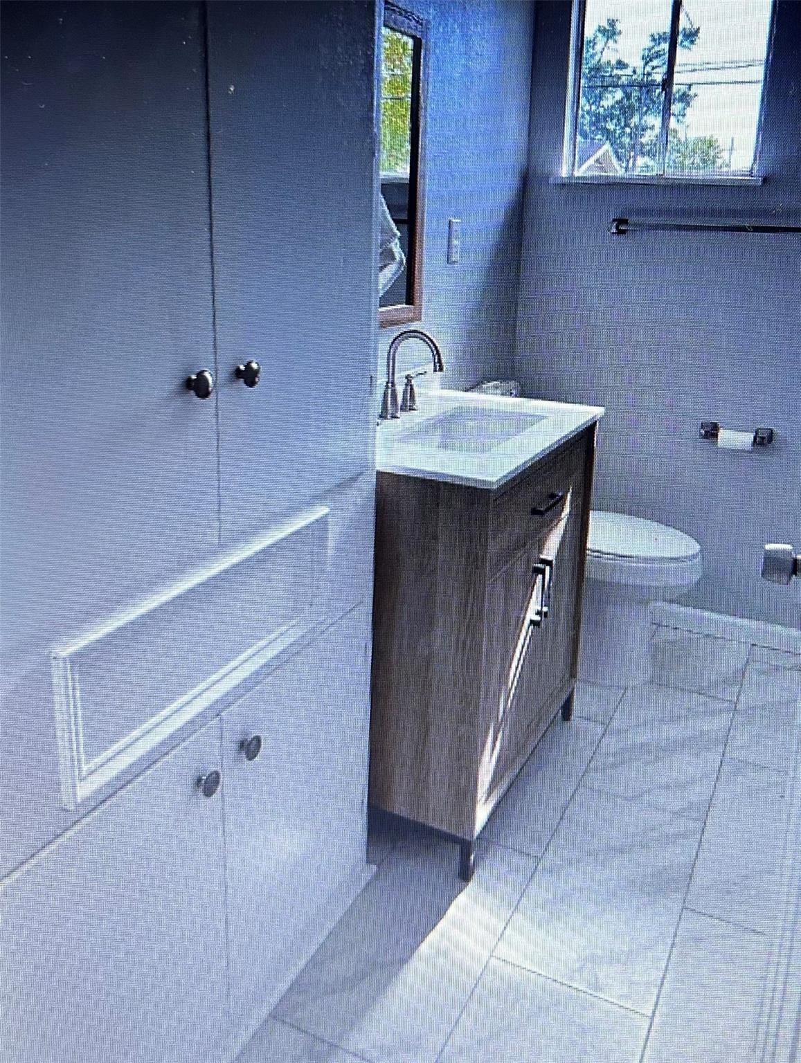 Bathroom with a dark wood vanity, white sink, tiled floor, and window above the toilet.