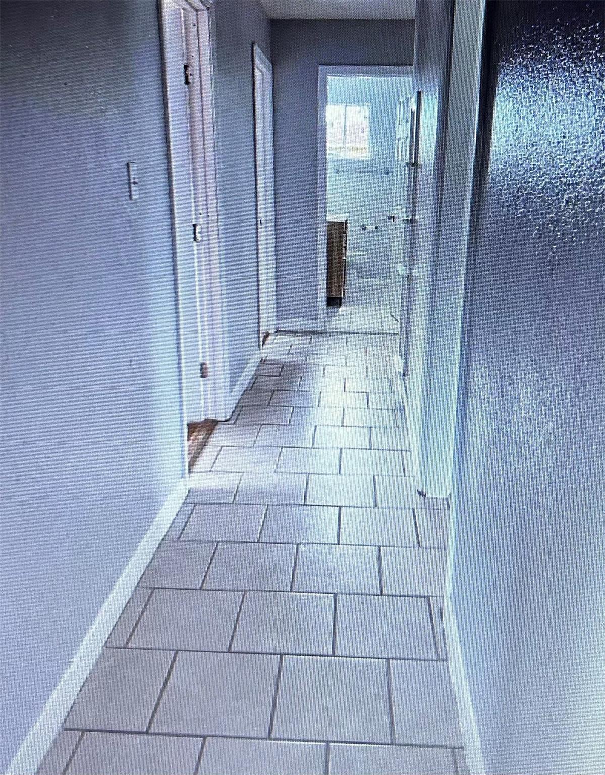Hallway with a light tiled floor and an open textured-glass door leading to a bathroom.