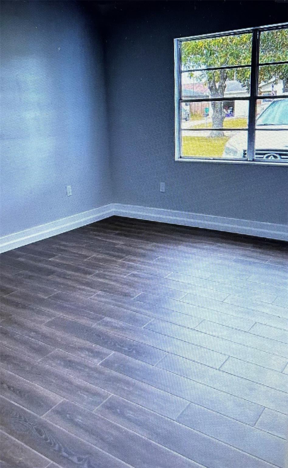 Vacant room with dark plank flooring and a large divided window.