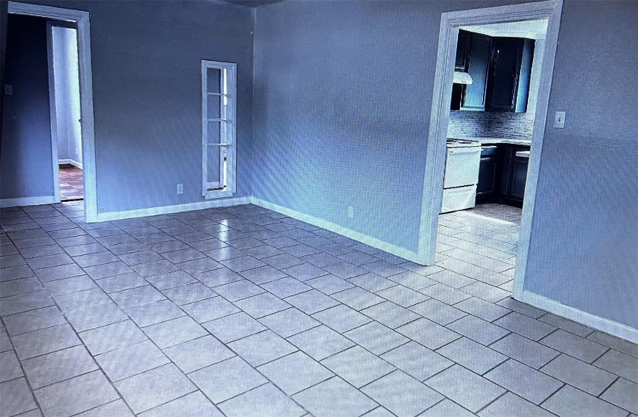 Empty tiled room with blue-gray walls, a narrow window, and a view into the kitchen.