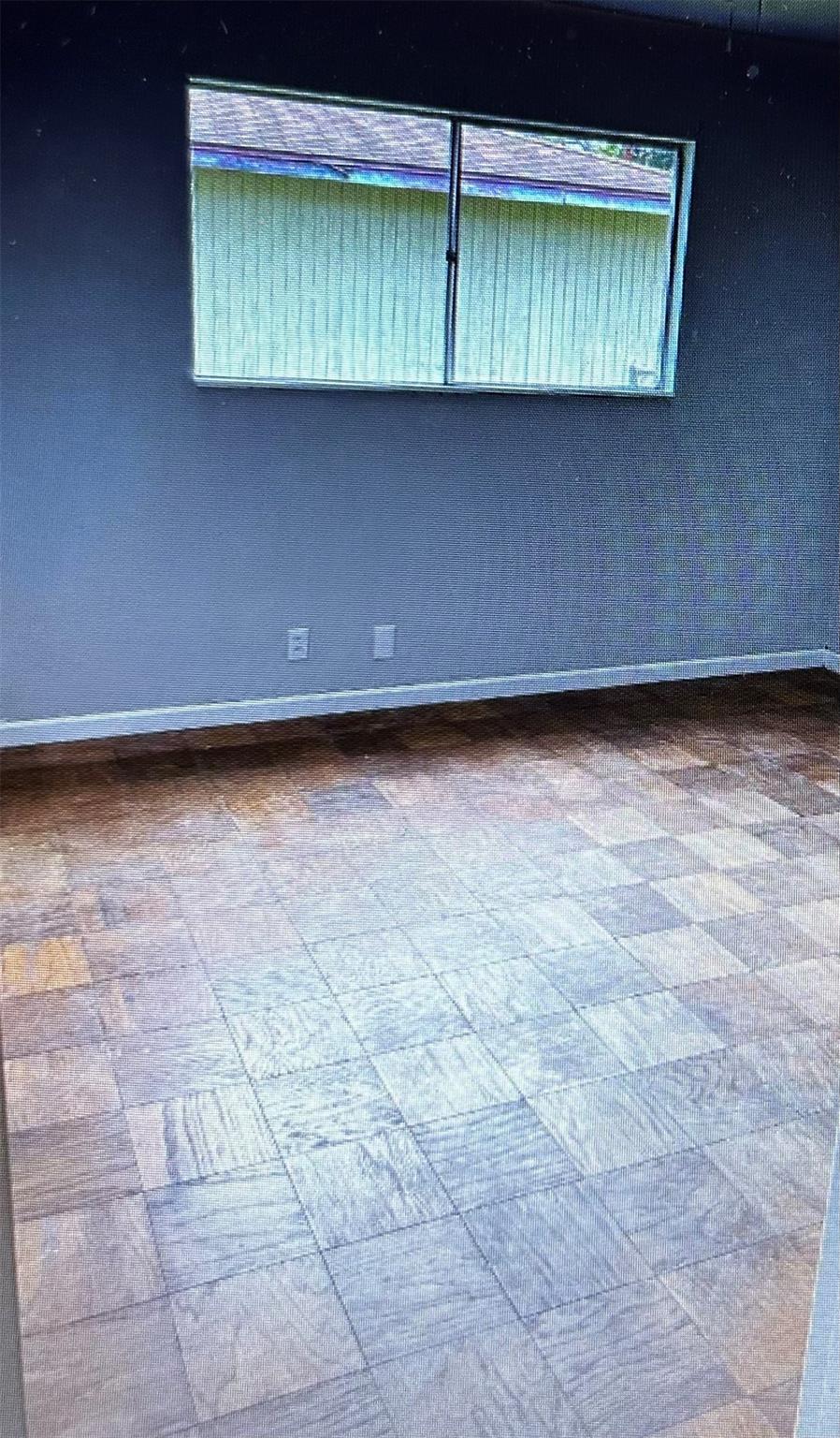 Empty room with a window and closed blinds above multicolored tile flooring.