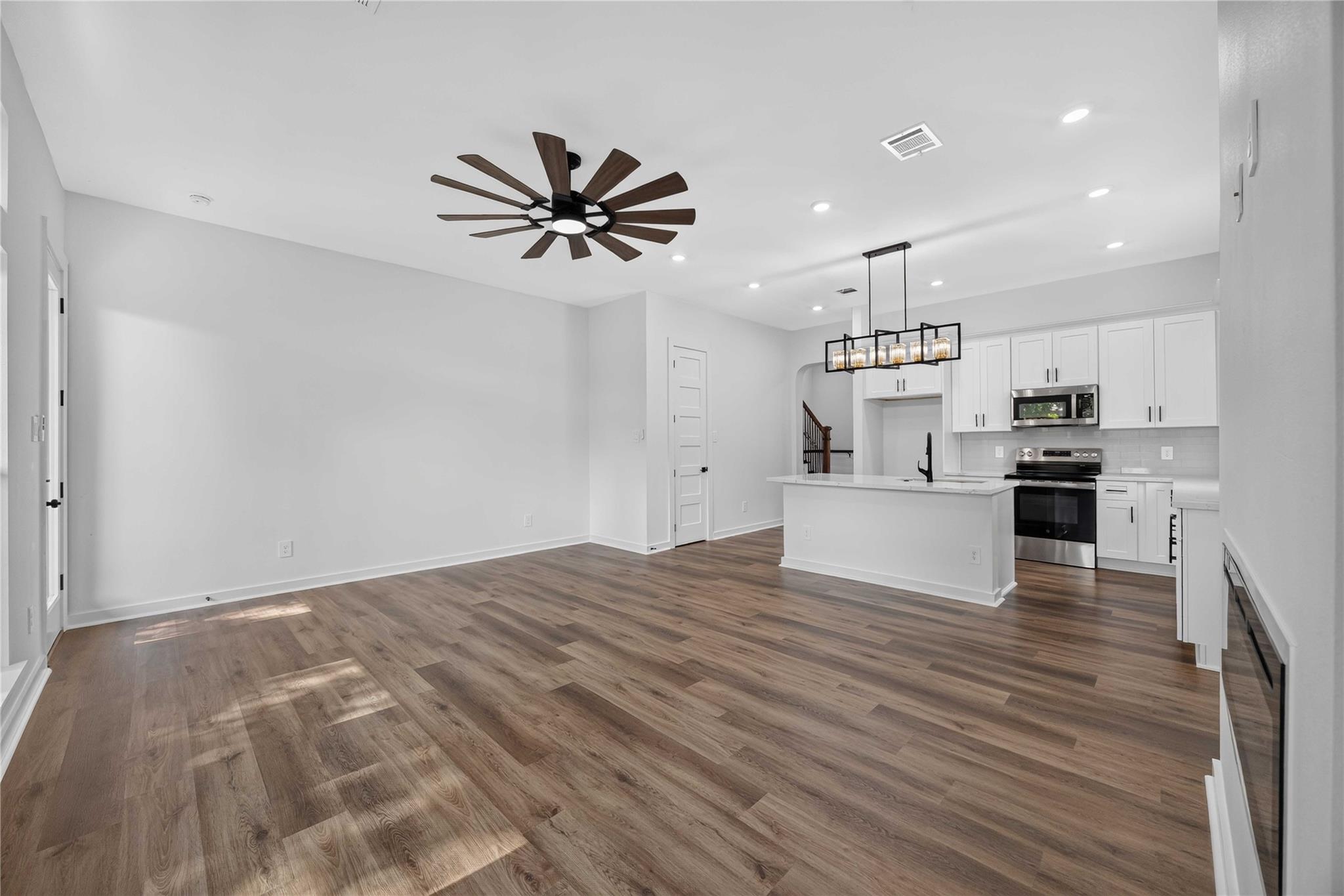Open-plan living area and white kitchen with wood-look floors, island, and oversized ceiling fan.