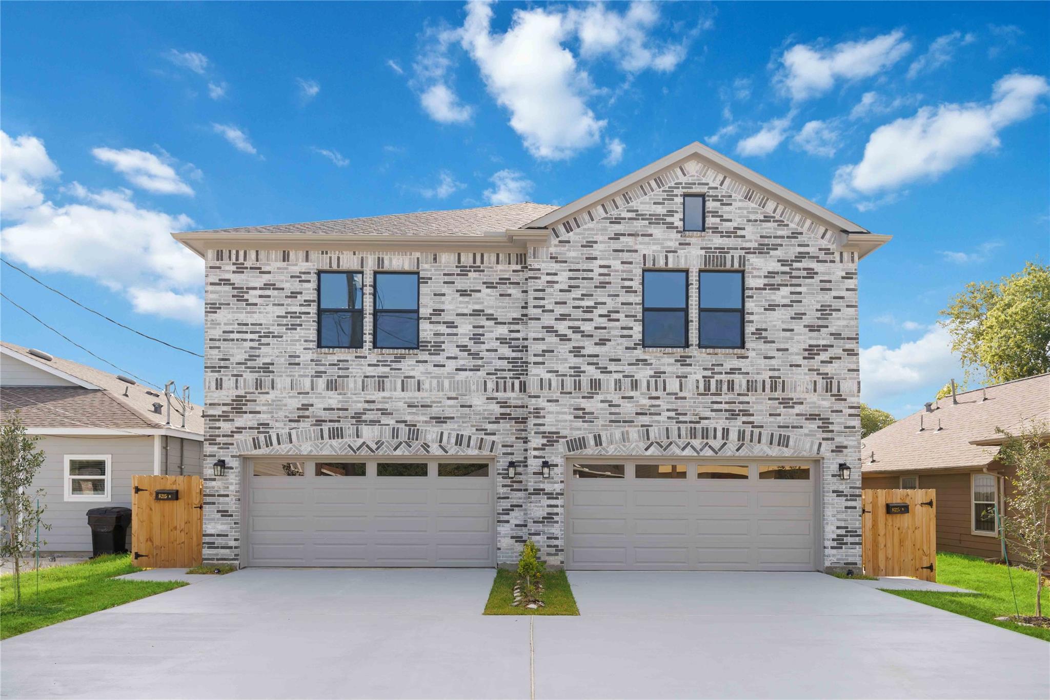 Two-story brick duplex with matching garages, separate driveways, and wooden side gates.