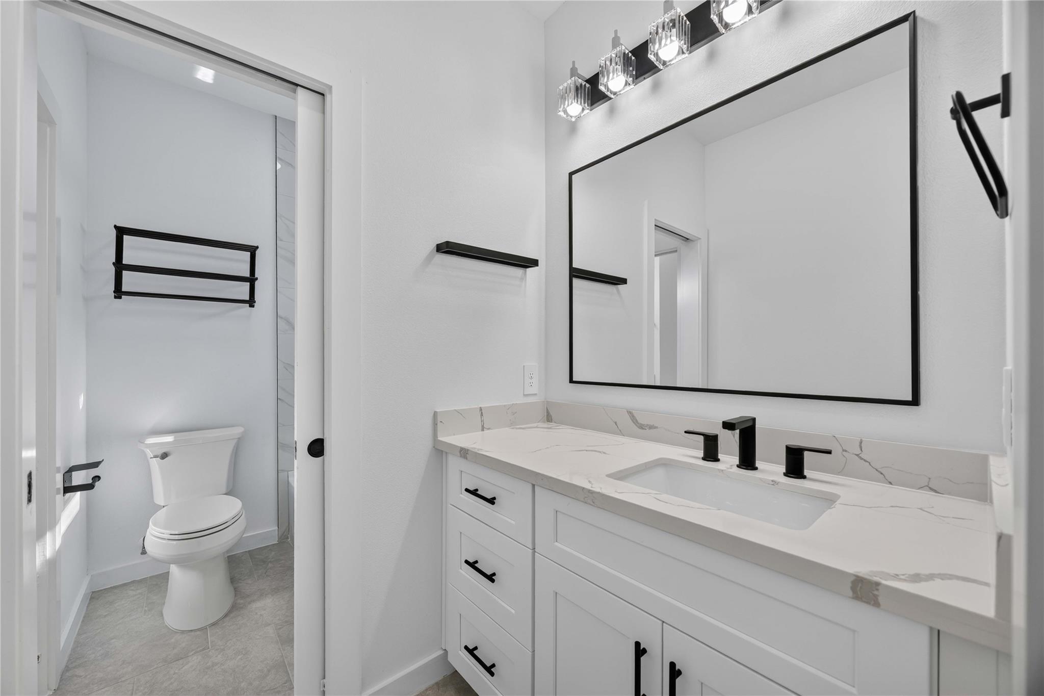 Modern bathroom with a veined white vanity, black fixtures, and a toilet in a separate alcove.