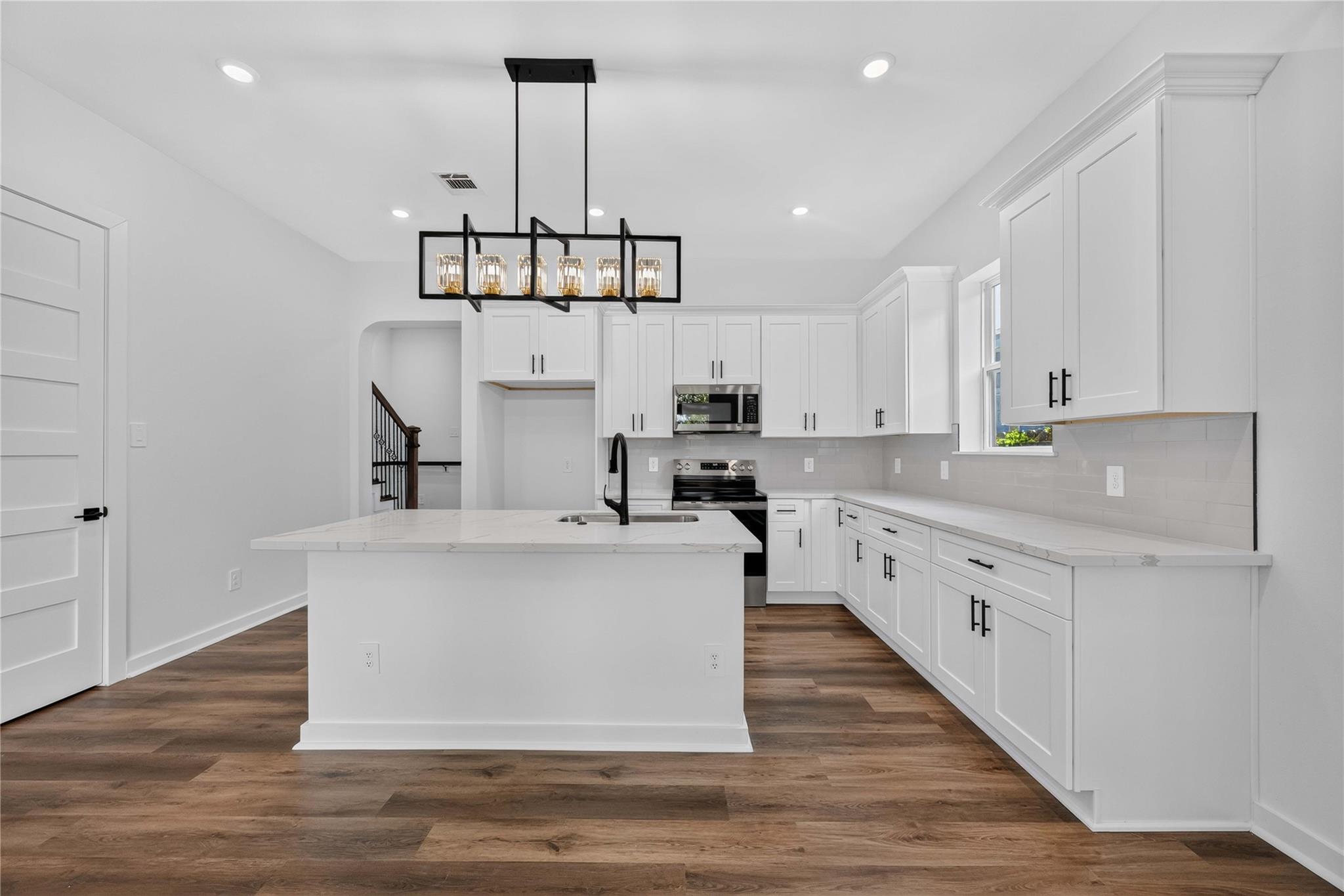 Bright kitchen with white shaker cabinets, a quartz island, stainless appliances, and brown wood-look floors.