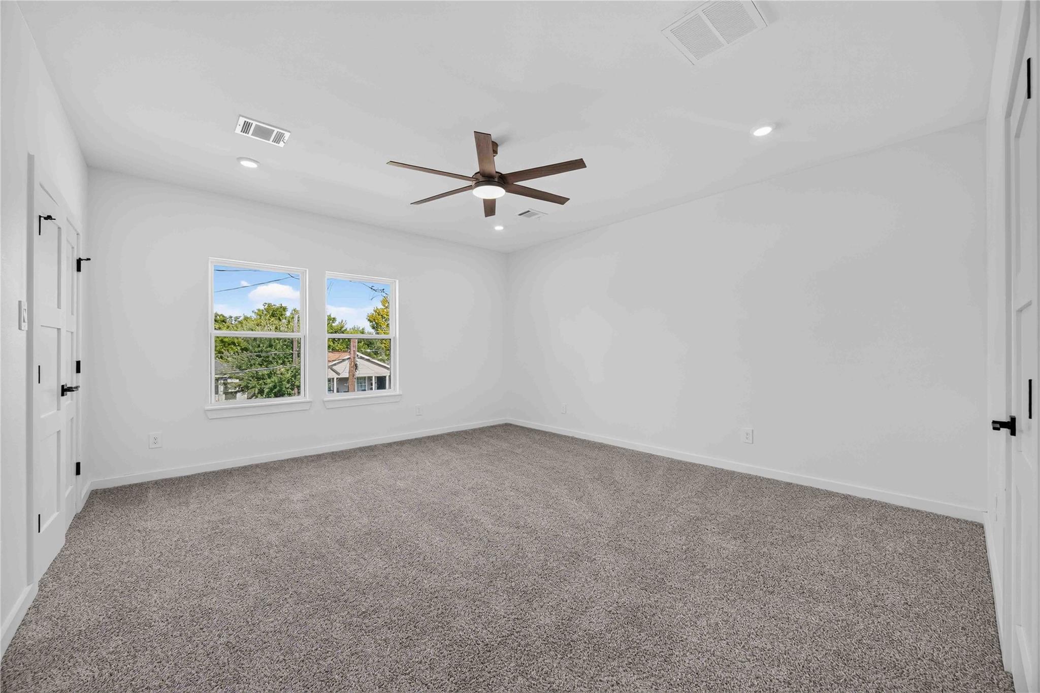 Empty bedroom with gray carpet, two windows, and a dark wood ceiling fan.