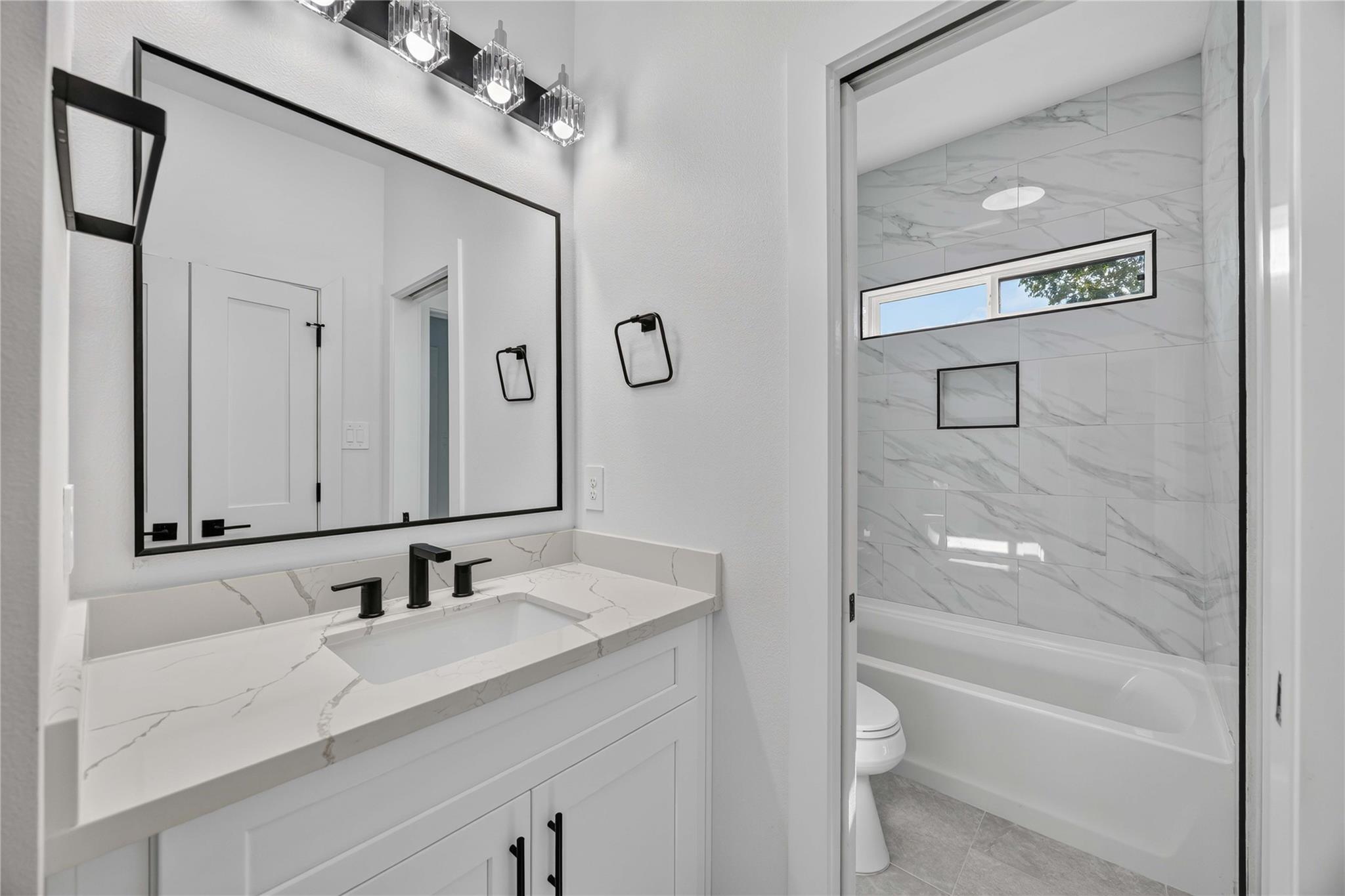 Bathroom with a veined vanity countertop and marble-look tile around the bathtub.