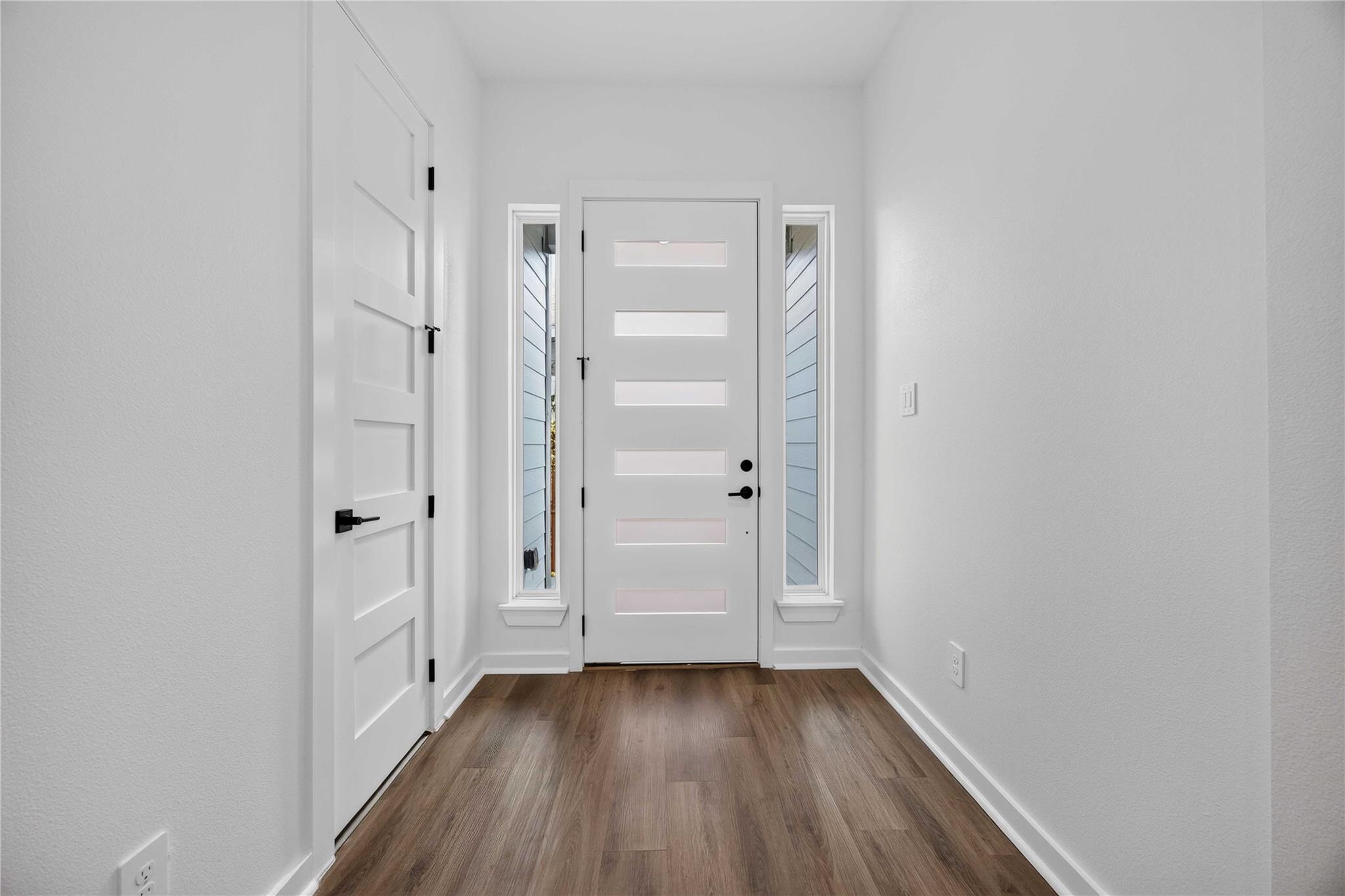 Entry foyer with a white front door, narrow sidelights, and brown wood-look flooring.