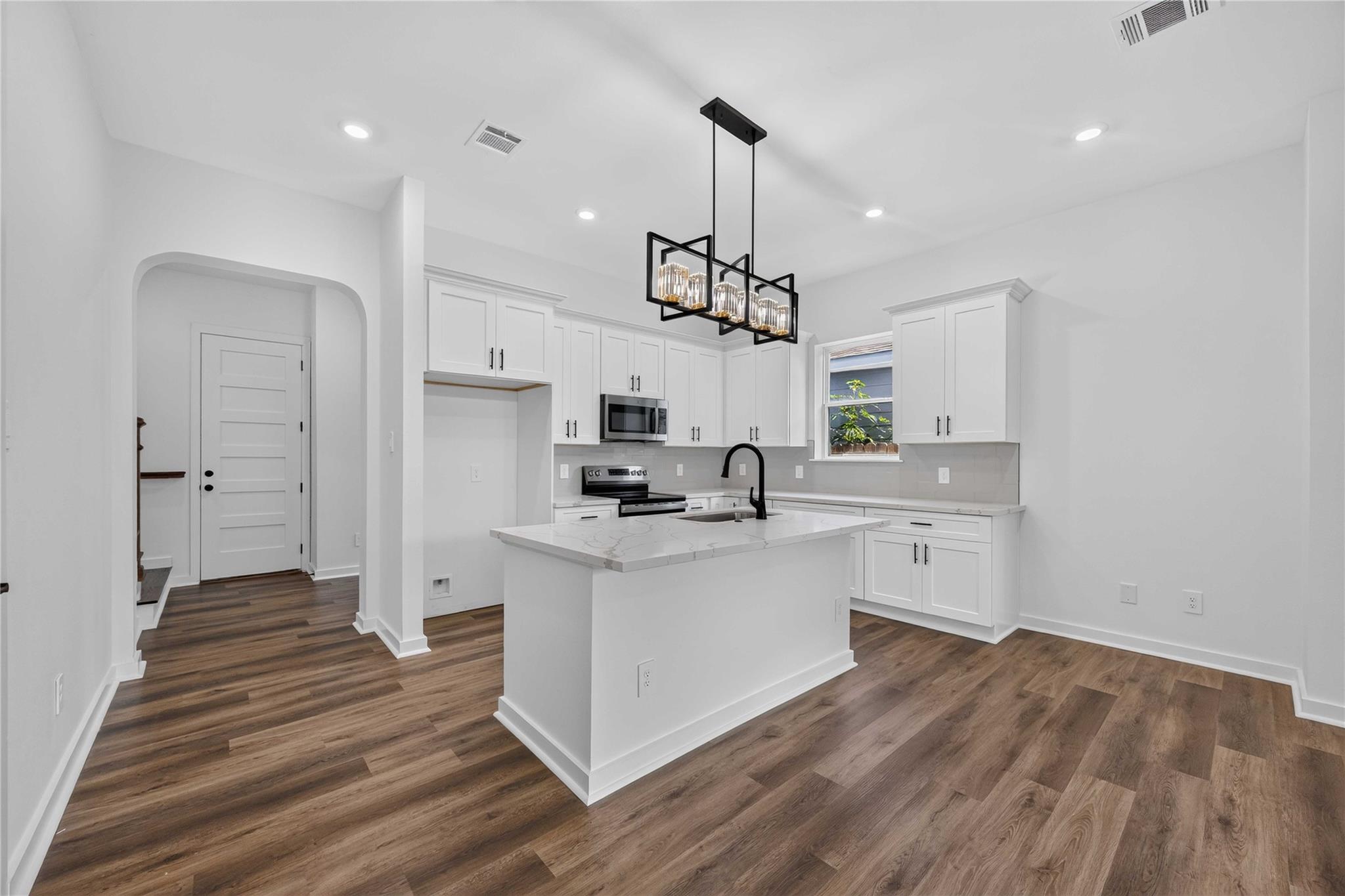 Vacant kitchen with white cabinets, a large island, stainless steel appliances, and wood-look flooring.
