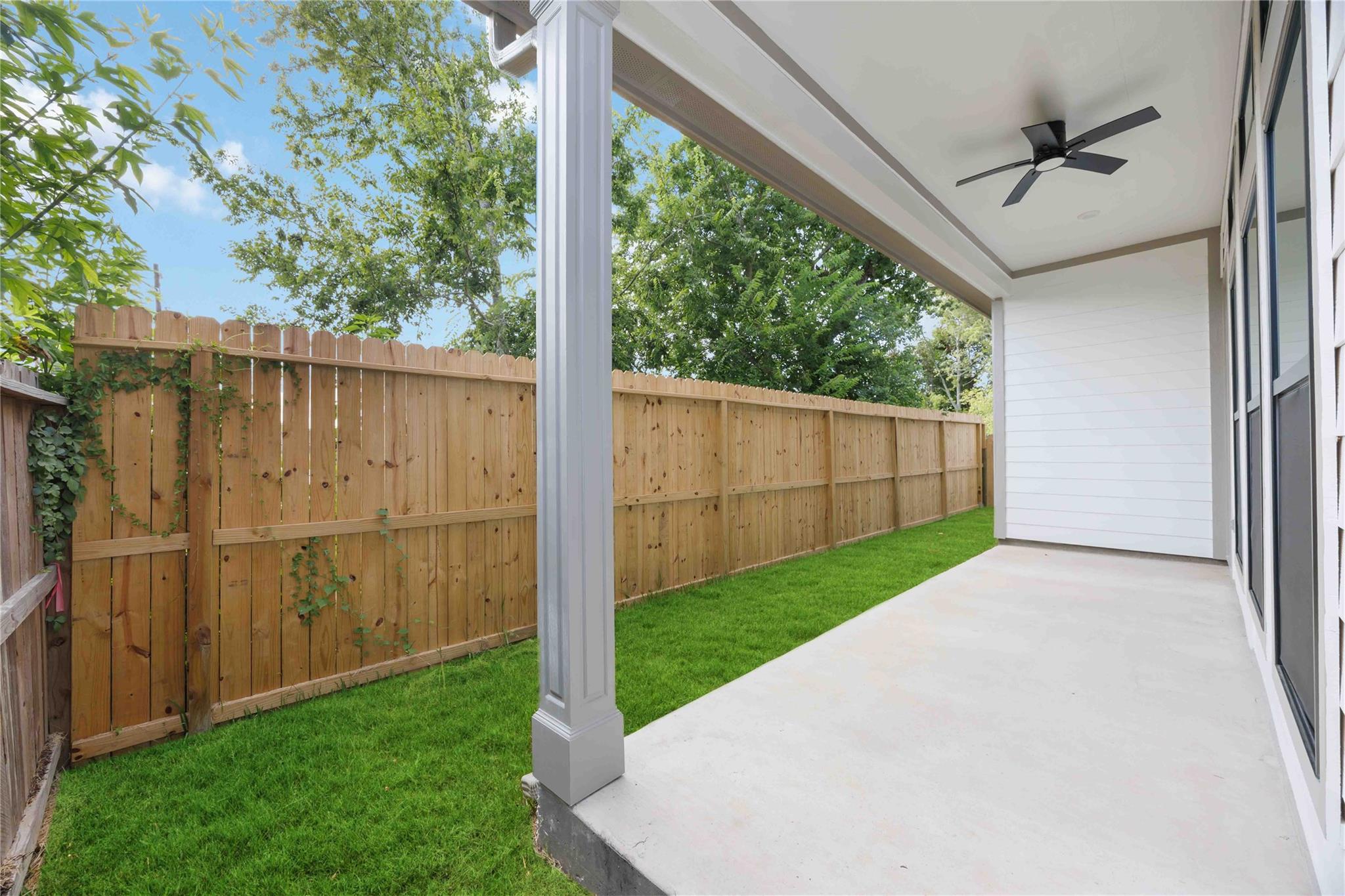Covered patio with a ceiling fan beside a fenced, grassy backyard.