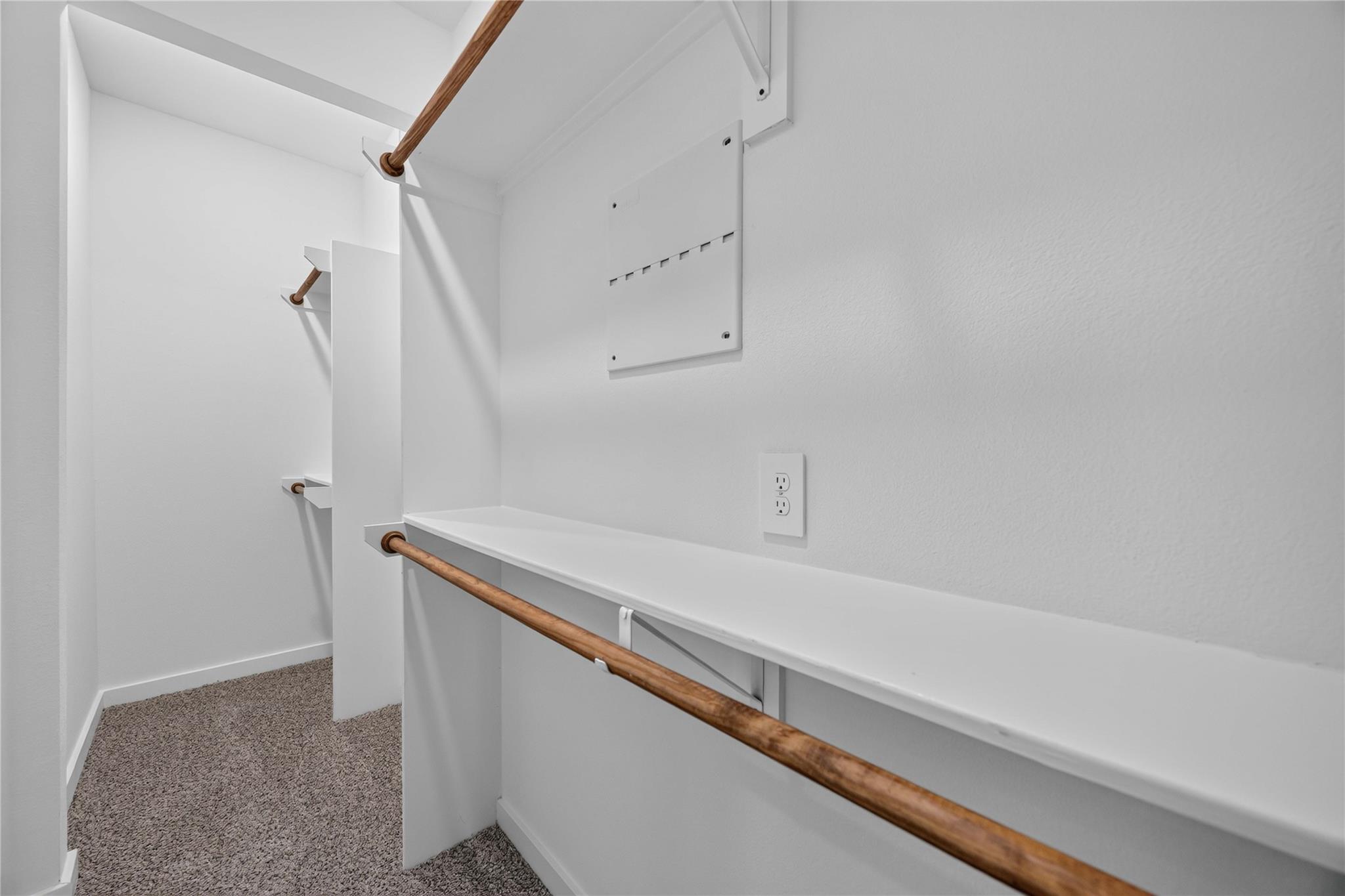 Empty walk-in closet with white shelving, wooden hanging rods, and gray carpet.