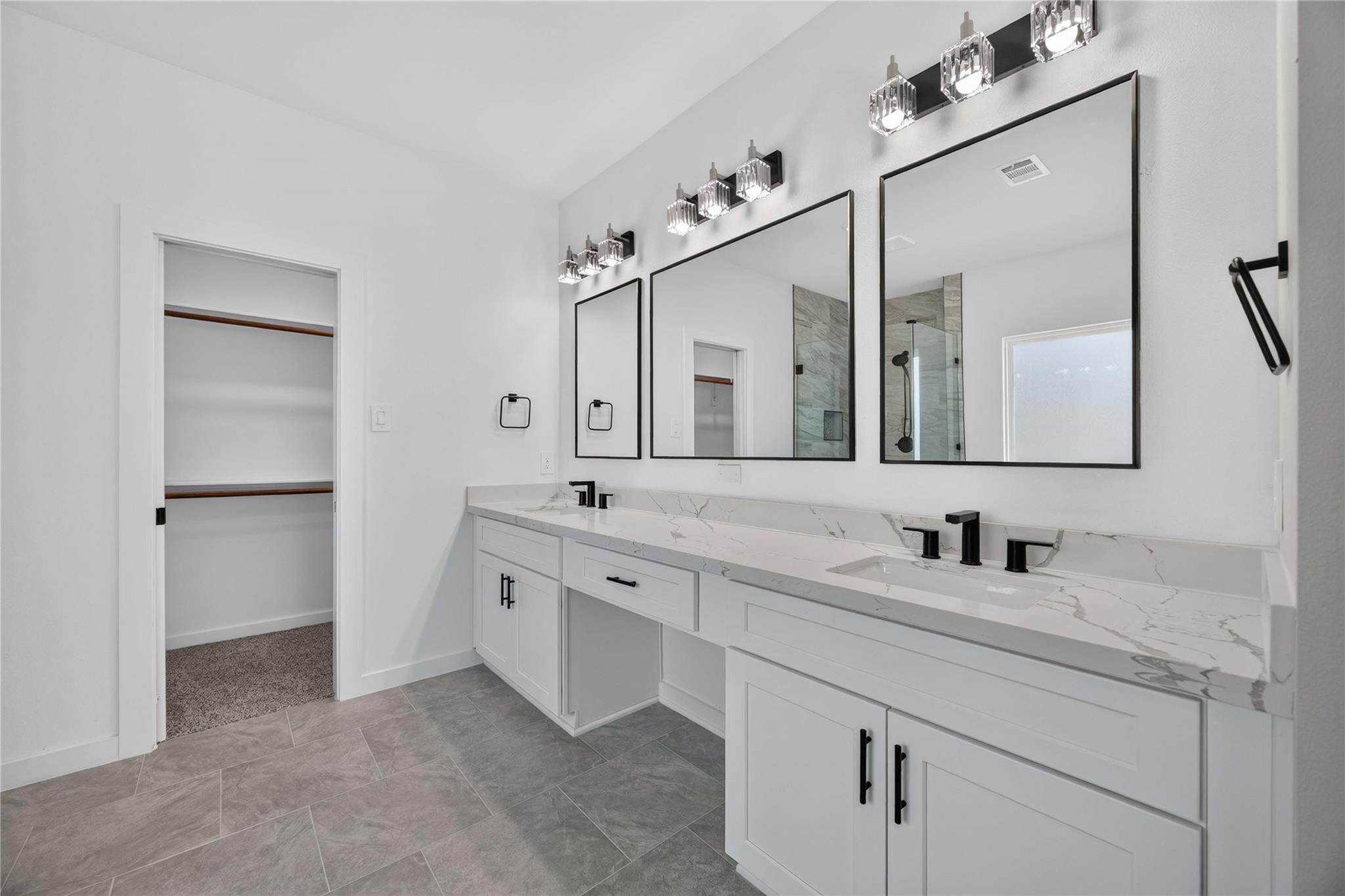 Bathroom with a white double vanity, veined countertop, black faucets, and three framed mirrors.
