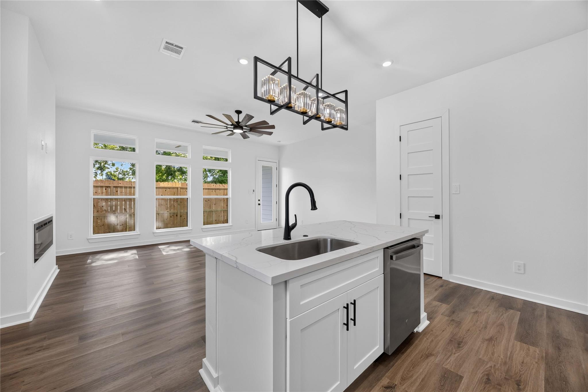 Bright kitchen with a quartz island, black faucet, pendant light, and windows overlooking a fenced yard.