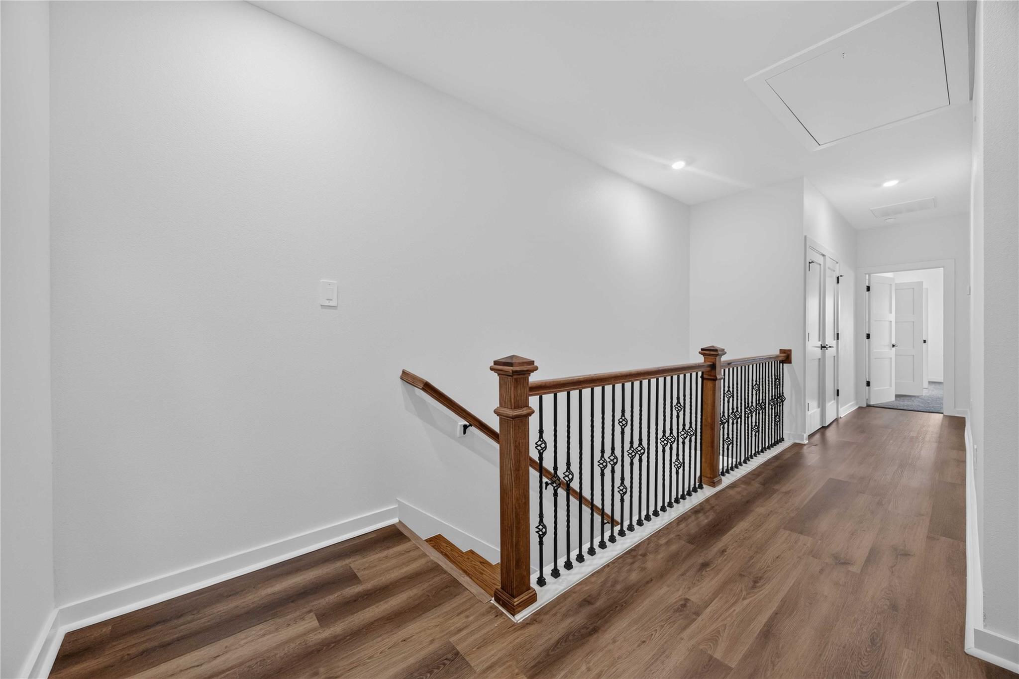 Upstairs hallway with wood flooring and a staircase with decorative metal railing and wooden posts.