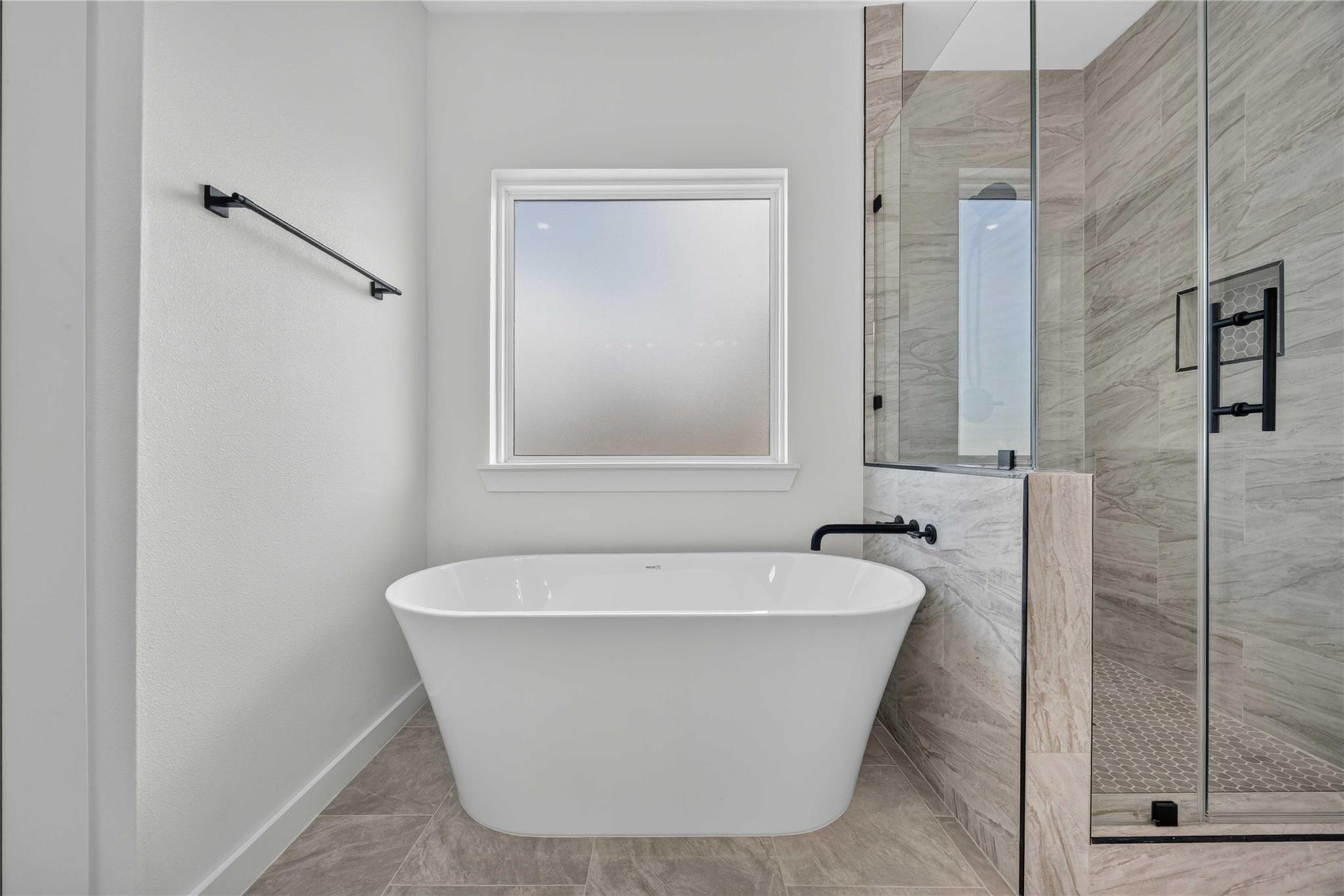 Bathroom with a freestanding soaking tub beside a tiled glass shower with black fixtures.